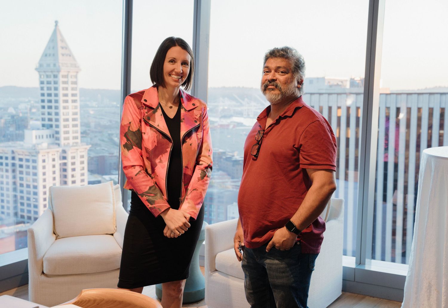 Two professionals stand together in a high-rise office with Seattle's iconic Space Needle visible through windows in background.