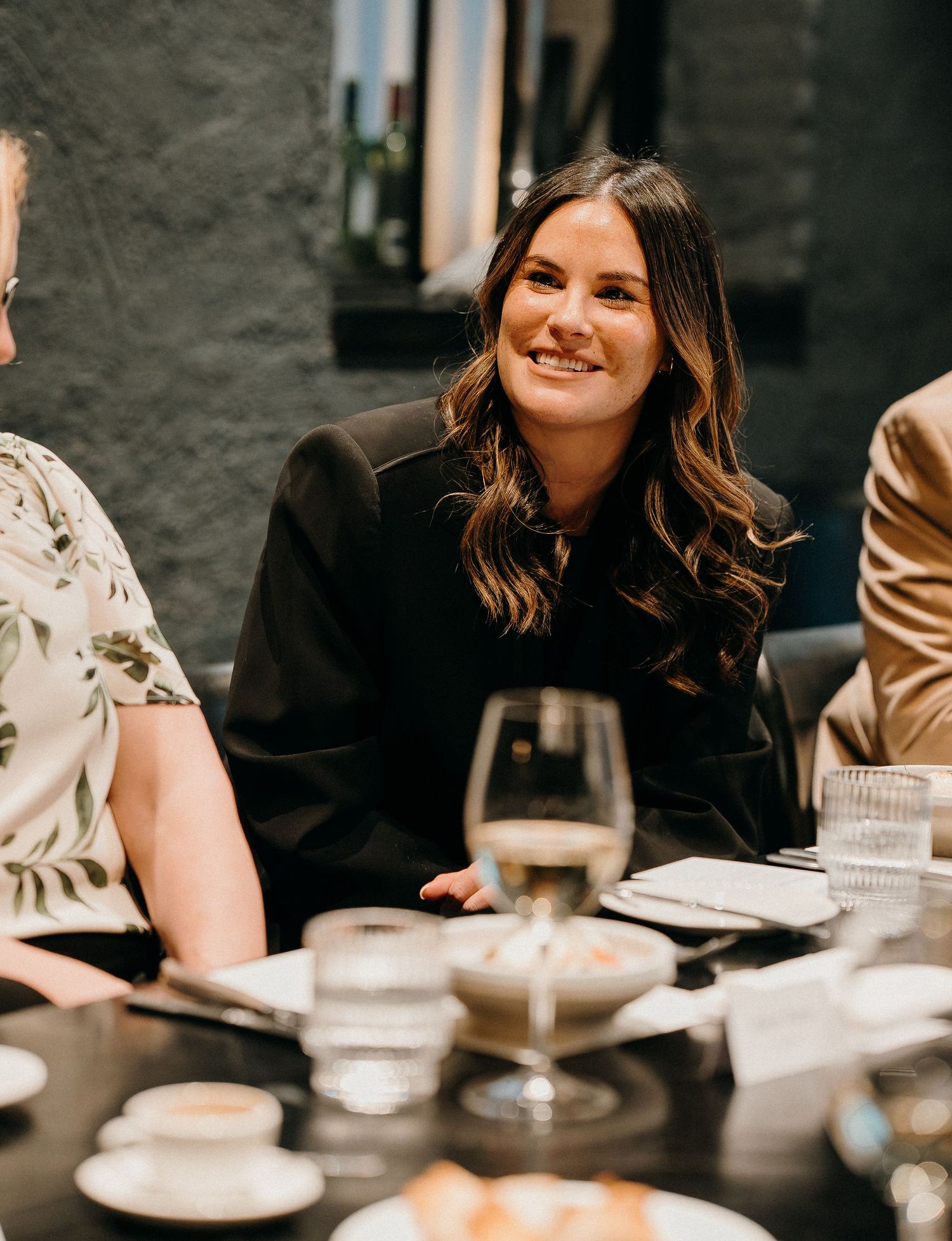 A group of friends enjoying dinner together at a dimly lit restaurant table with wine glasses and plates.