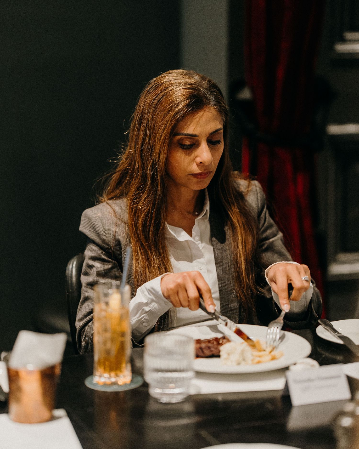 A person in business attire enjoys a meal at an upscale restaurant with dark decor and ambient lighting.