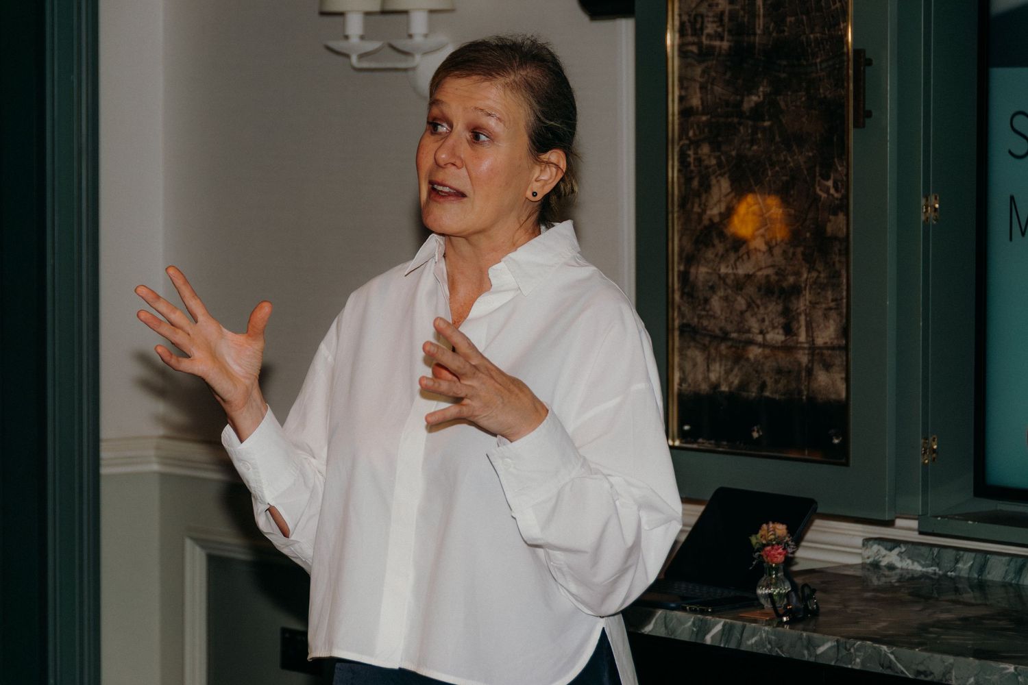 A person in a white chef's coat gestures expressively while speaking in what appears to be a restaurant setting.