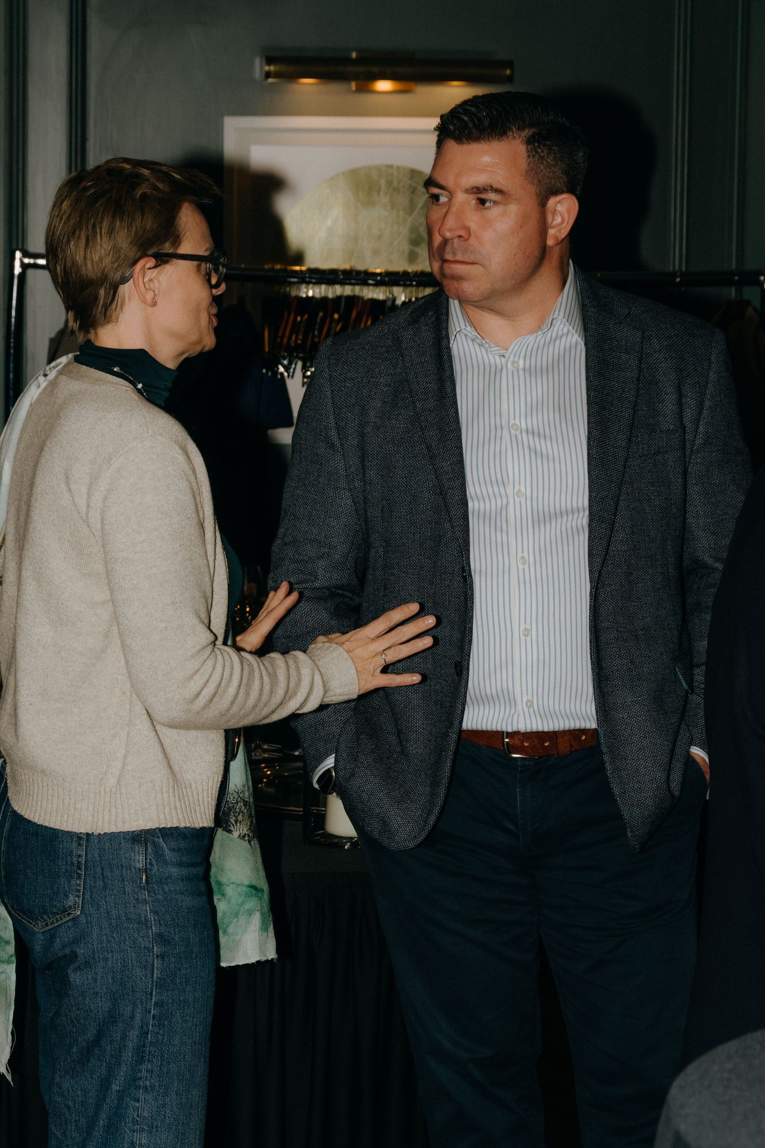 People in casual and business attire stand in a dimly lit room during what appears to be a social gathering.