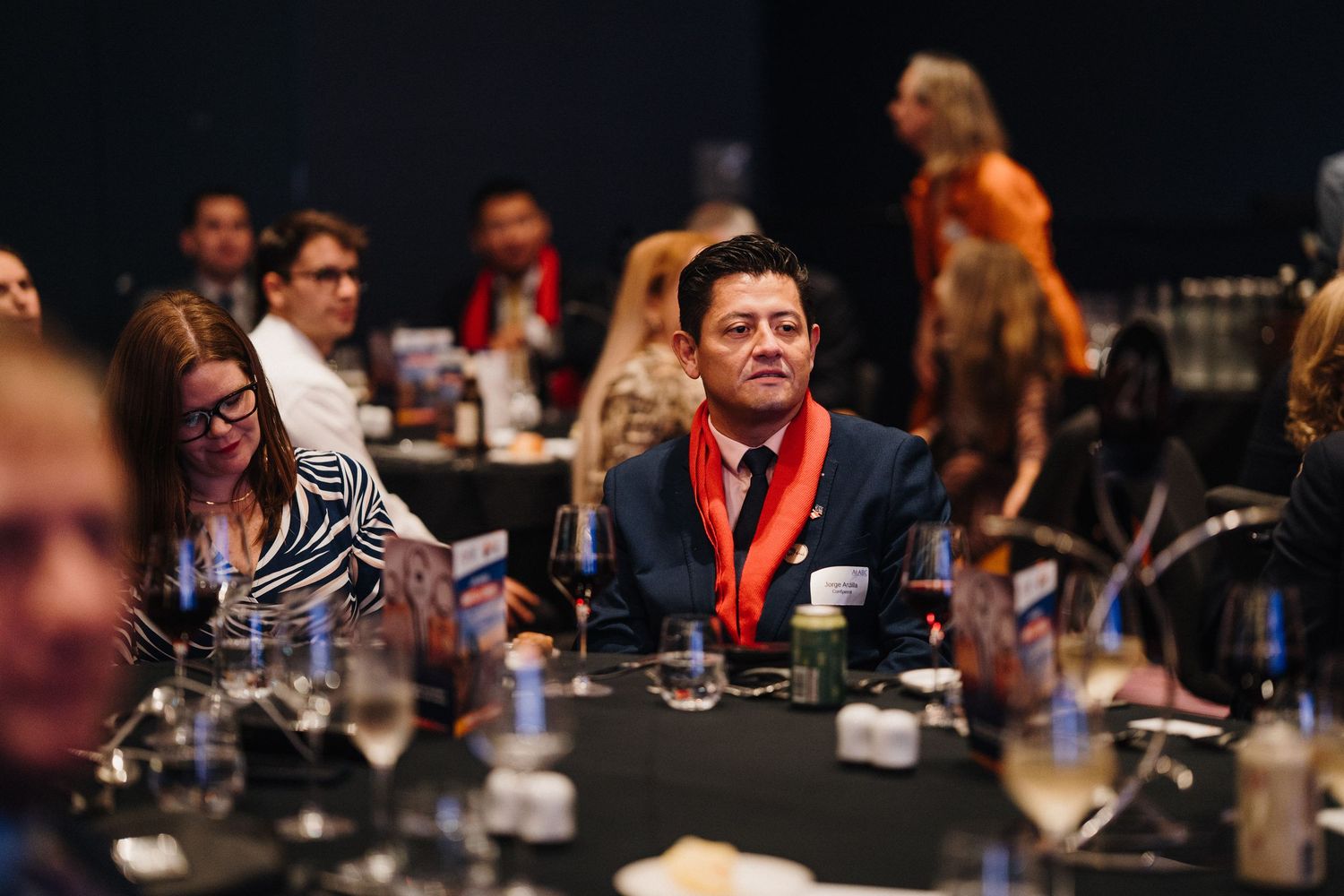 Business professionals engage in animated discussion during a corporate networking event at a dimly lit venue.