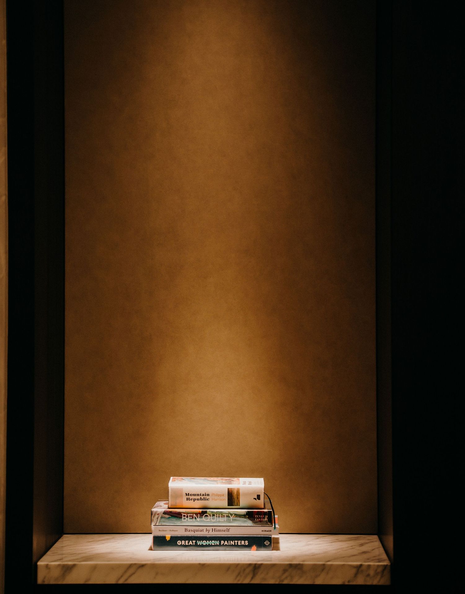 Stack of books illuminated by dramatic lighting on wooden surface against brown wall with moody atmosphere.