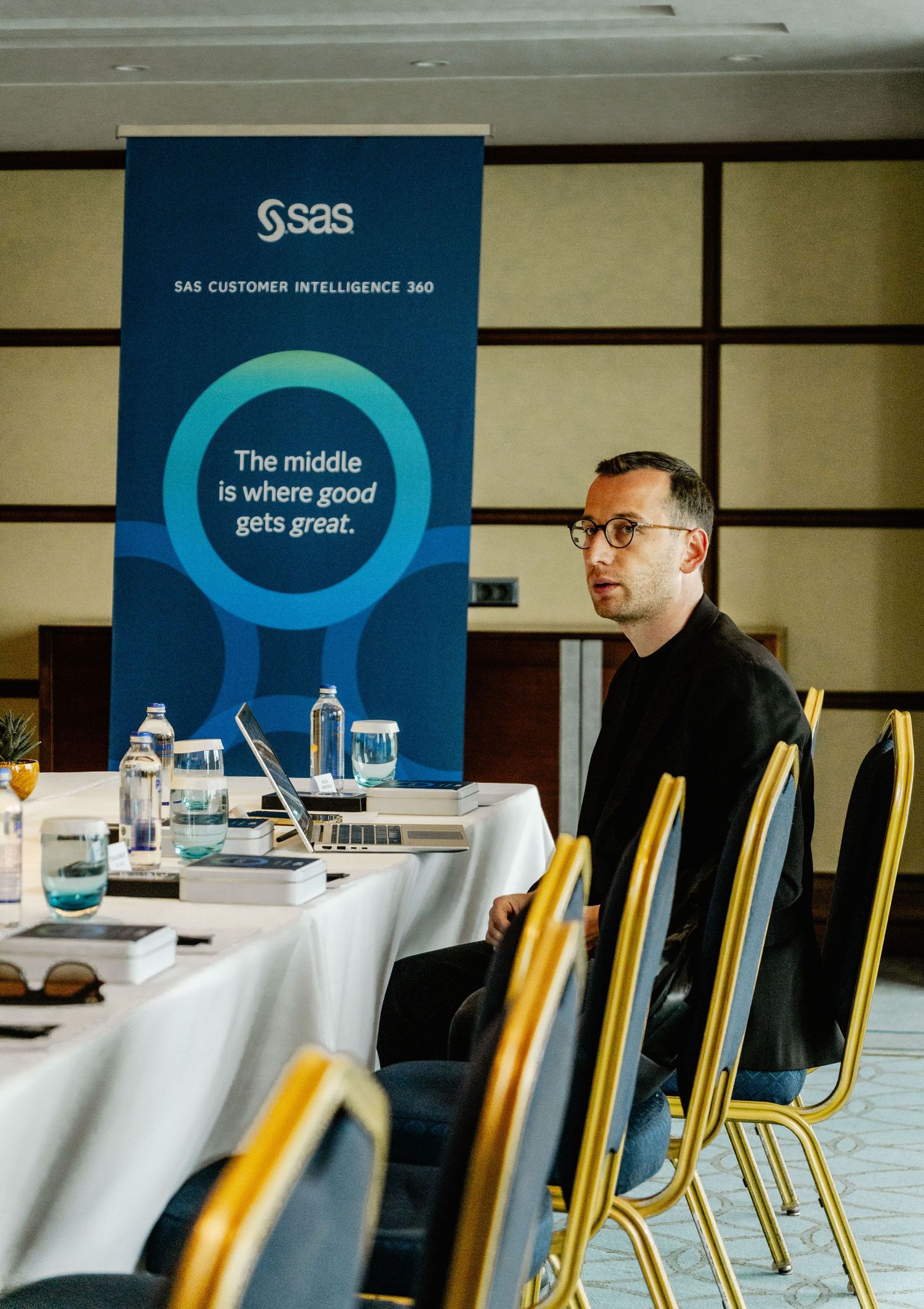 Man sitting at a conference table beside a SAS Customer Intelligence 360 banner reading The middle is where good gets great.