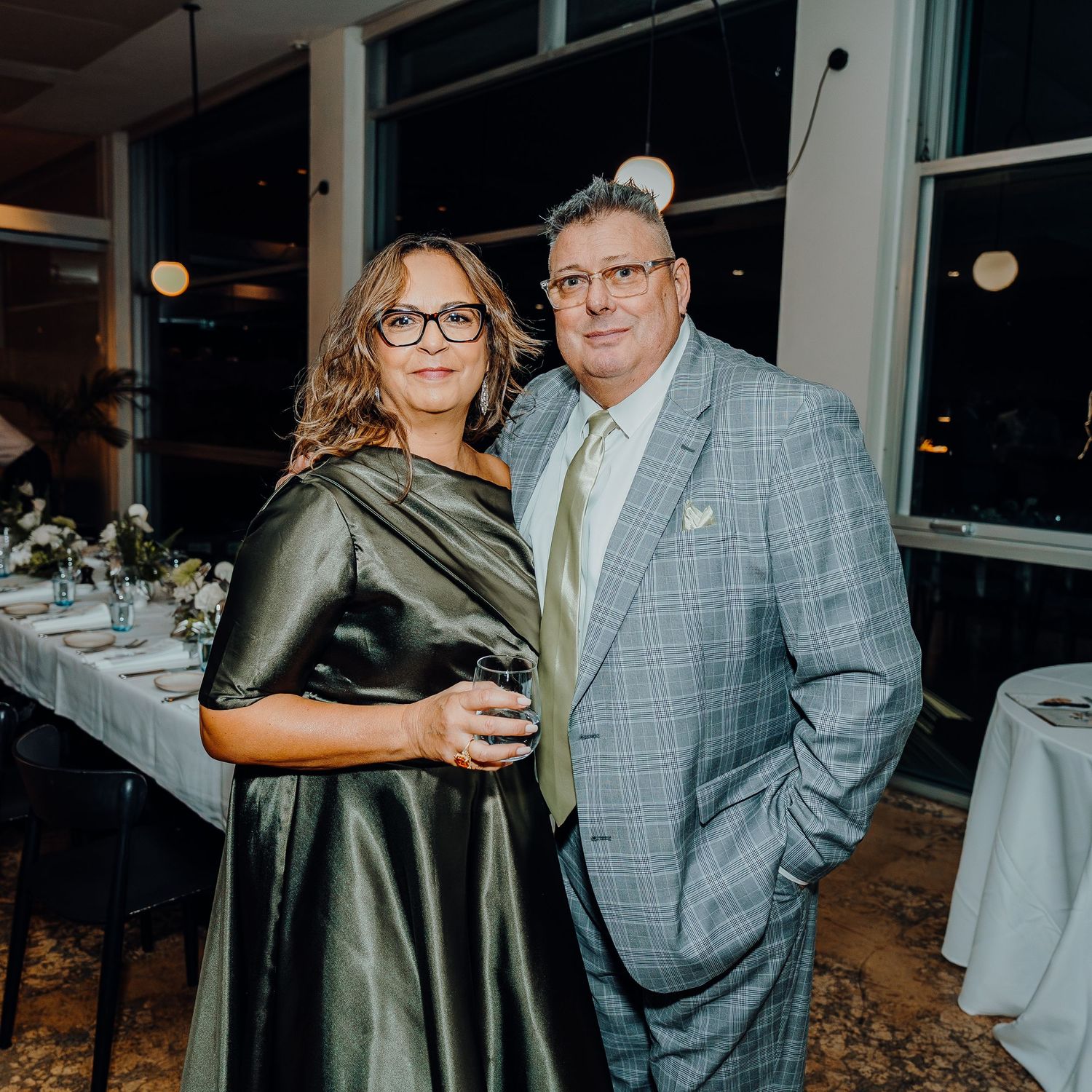A couple in formal attire enjoying an evening event, with the man wearing a gray plaid suit.