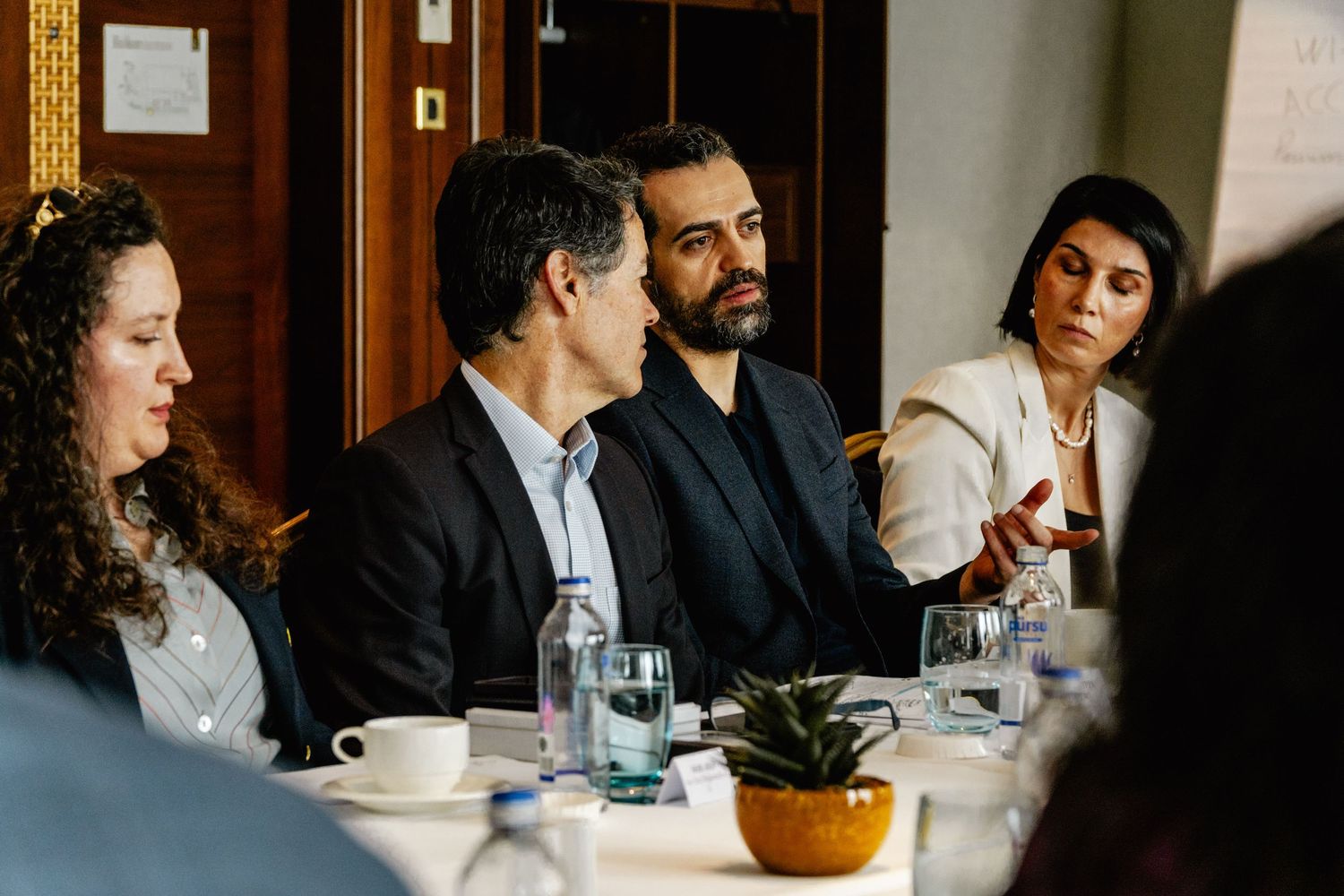 Four professionals engaged in discussion at a business lunch meeting around a white tablecloth dining table.