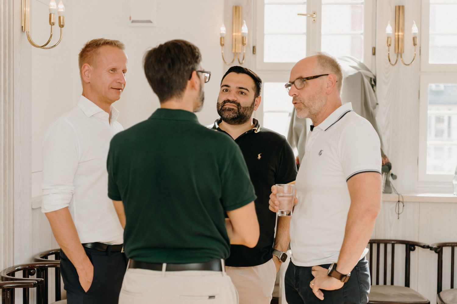 Four men in smart casual attire engaged in conversation at a bright, elegant indoor networking event.