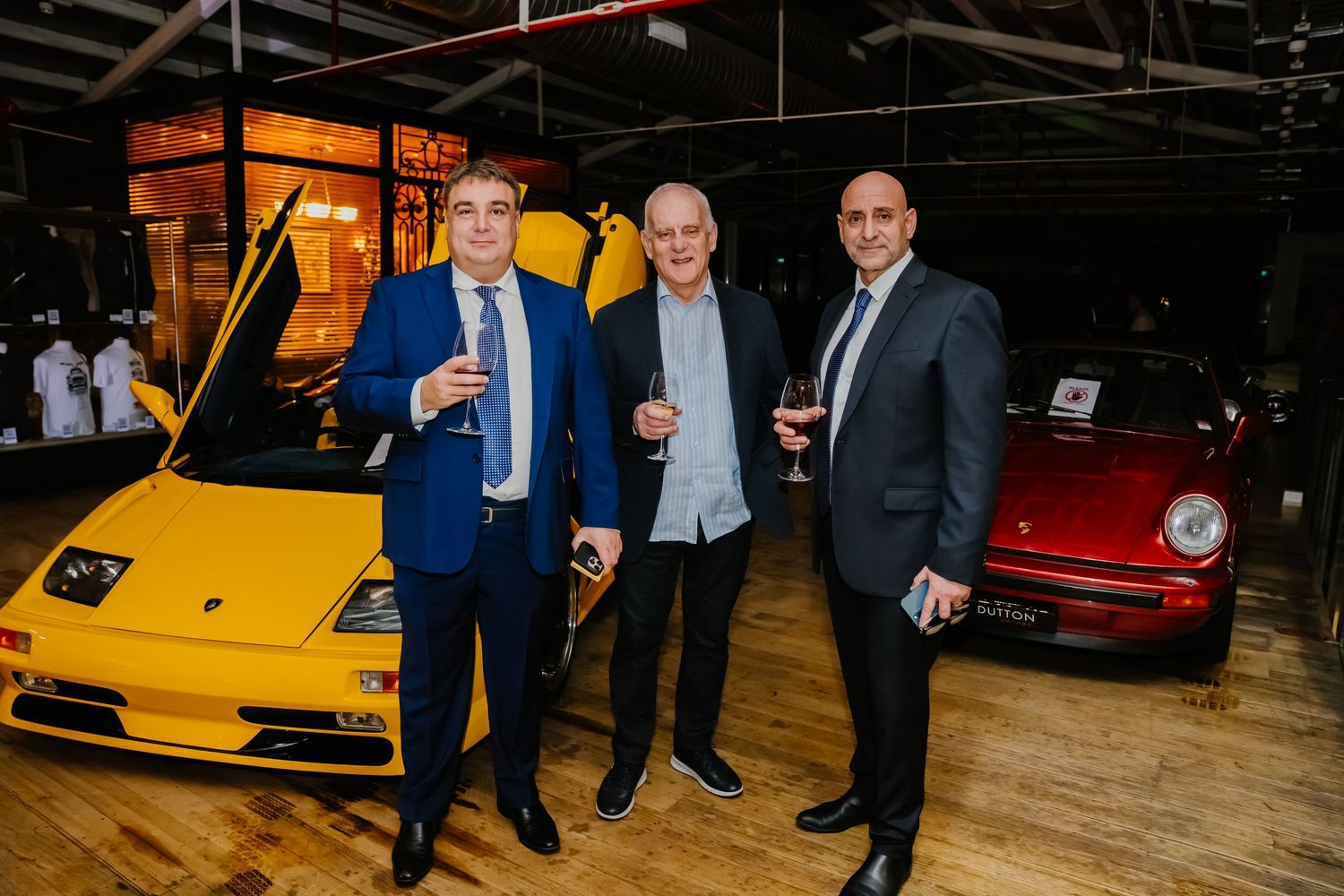 Red and yellow sports cars on display at an indoor auto show with attendees viewing the luxury vehicles.