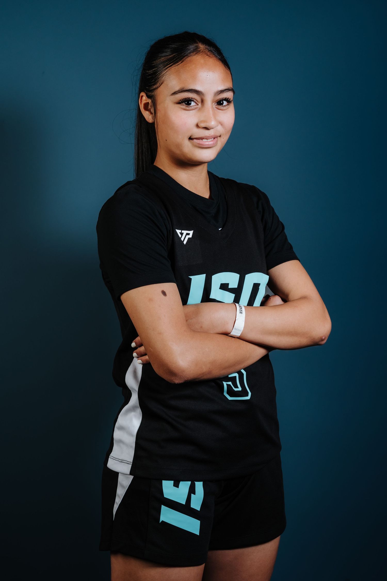 Athletic person wearing a black jersey with light blue lettering poses with arms crossed against a blue background.