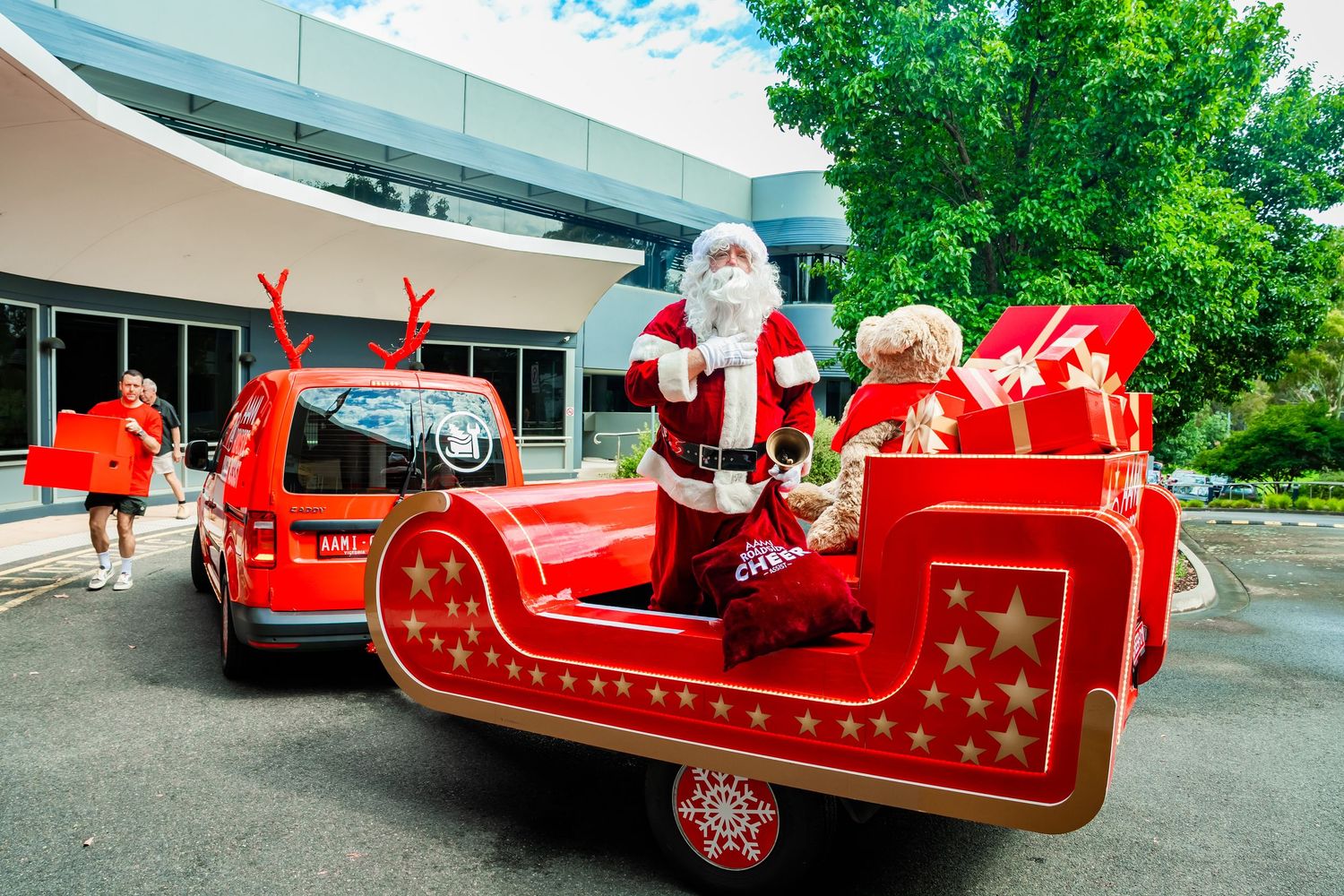 A bright red Christmas sleigh display with Santa and festive decorations parked outside a commercial building.