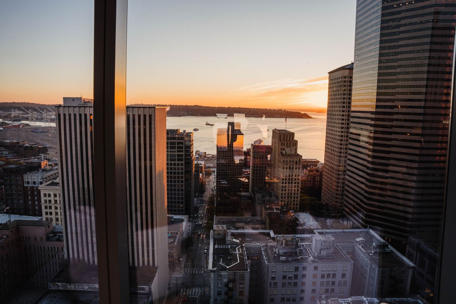 Aerial view of downtown Seattle skyline at sunset with skyscrapers and Elliott Bay in the background.