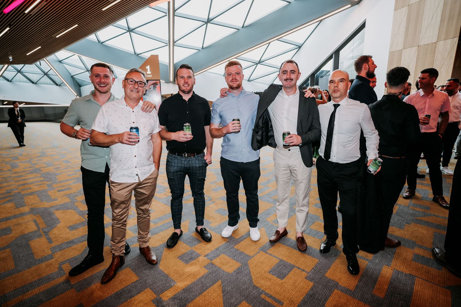 A group of guests in casual and semi-formal attire stand together holding drinks at a corporate event.