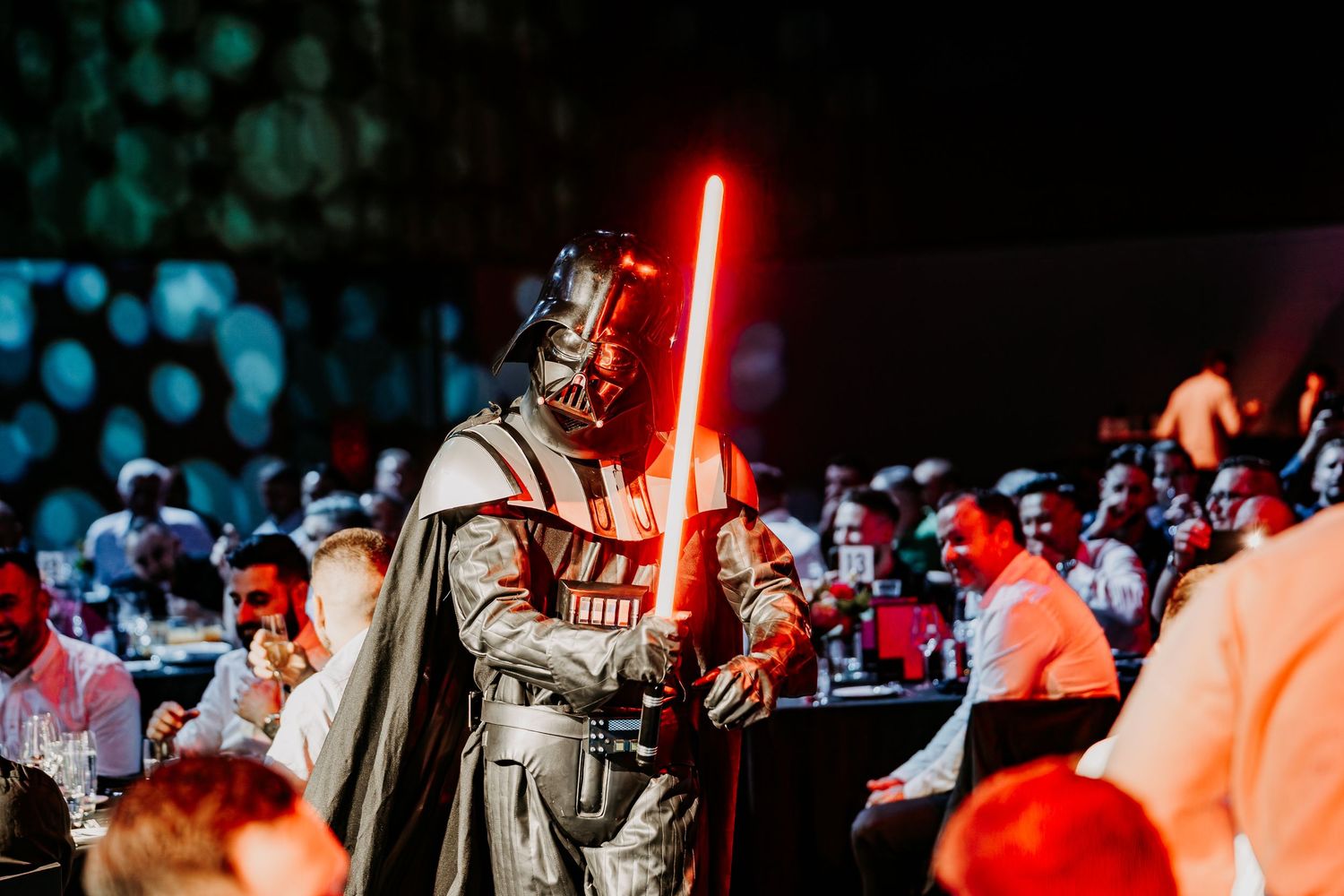 Star Wars cosplayers with red lightsabers perform battle scenes at a convention in dramatic lighting.