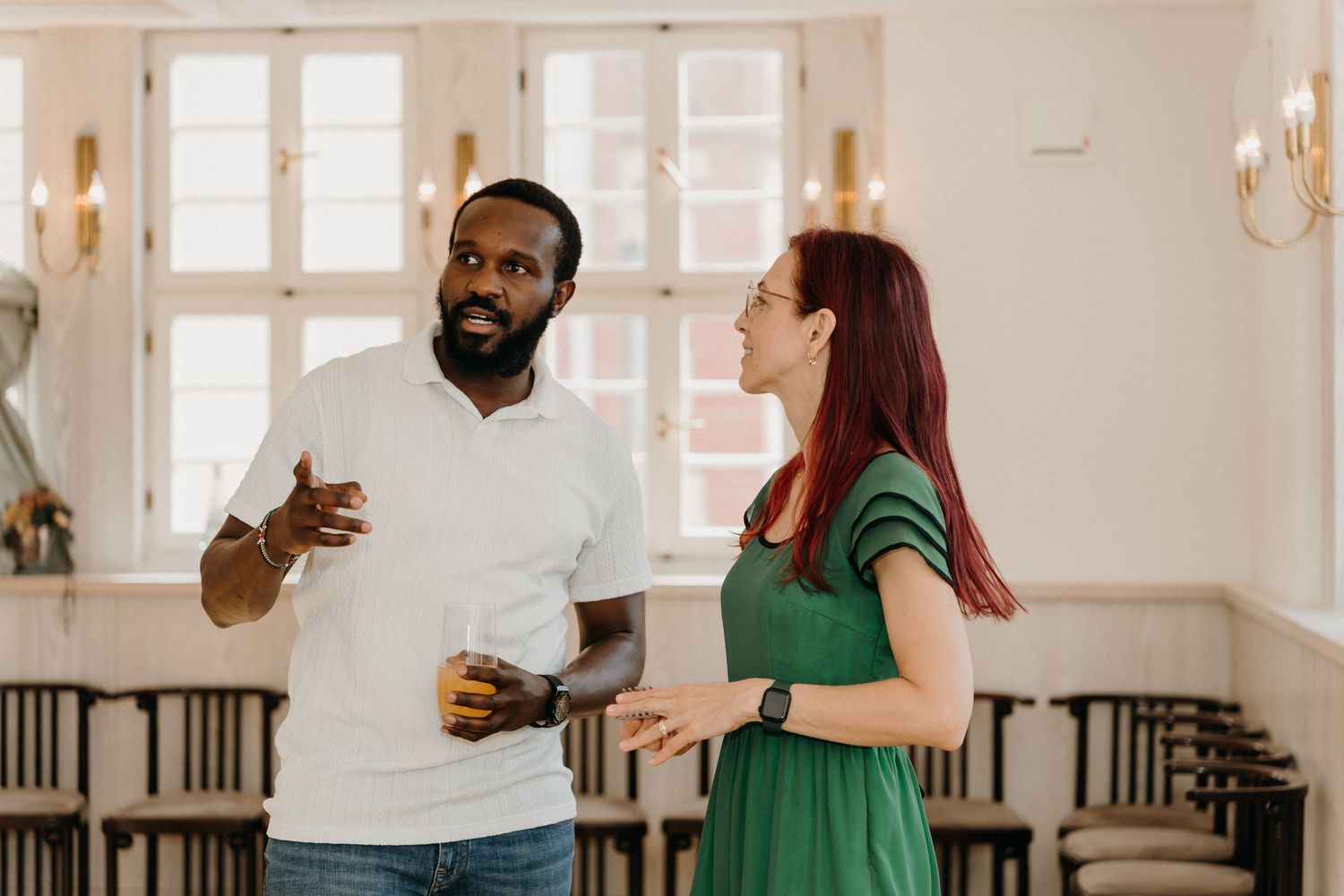 A Black man and a redhead woman in green dress having a conversation in an elegant bright room.
