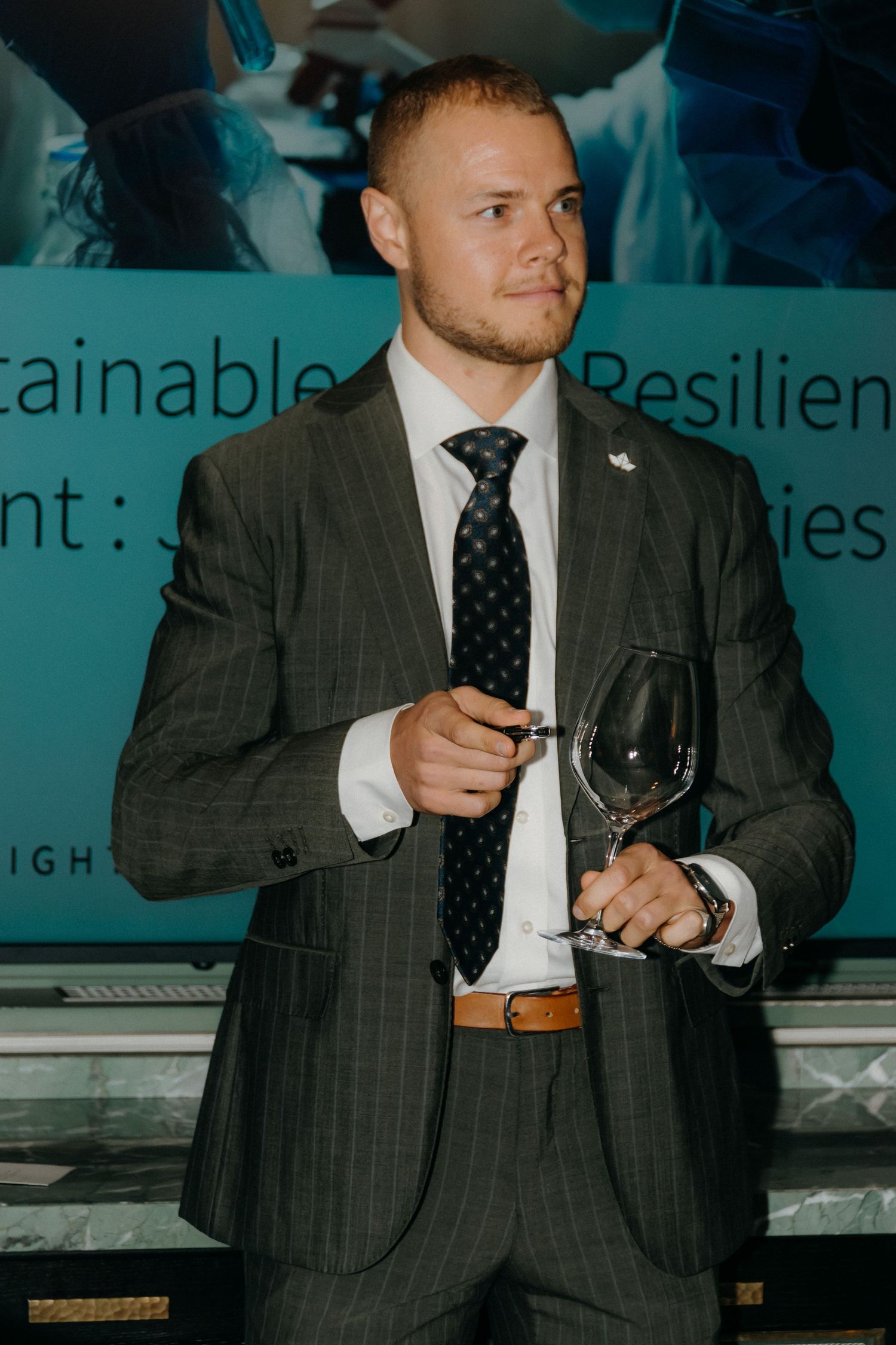 Professional in dark pinstriped suit and tie holds wine glass at formal business event.