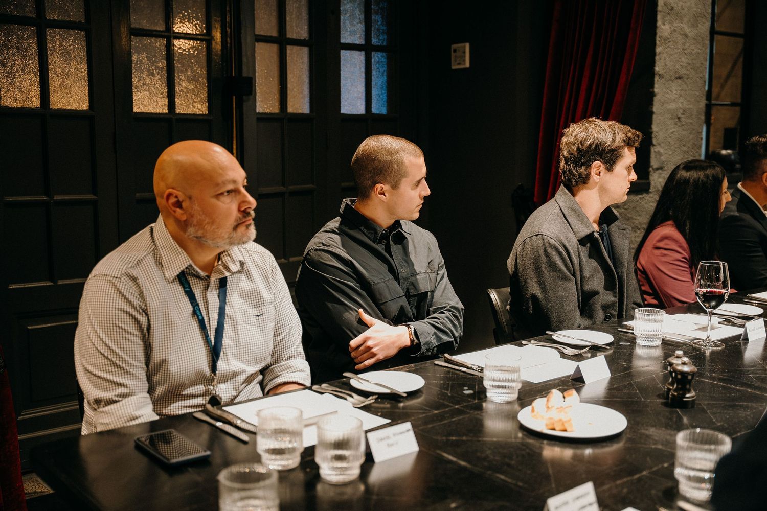 A group of people sit at a long table in a restaurant during a business meeting or dinner gathering.