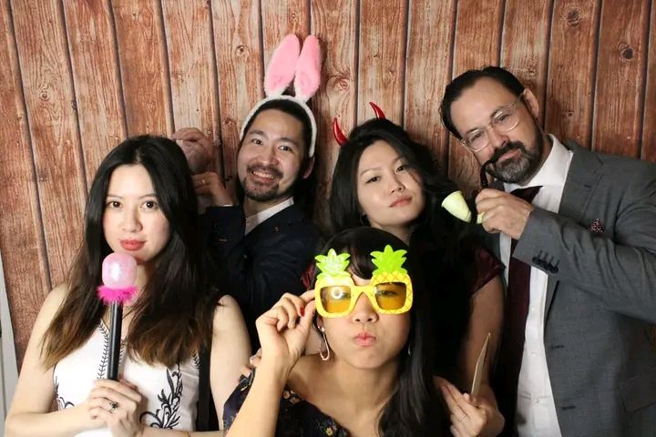 A photo strip from a party photo booth showing people posing with fun props and making silly faces against a wood background.