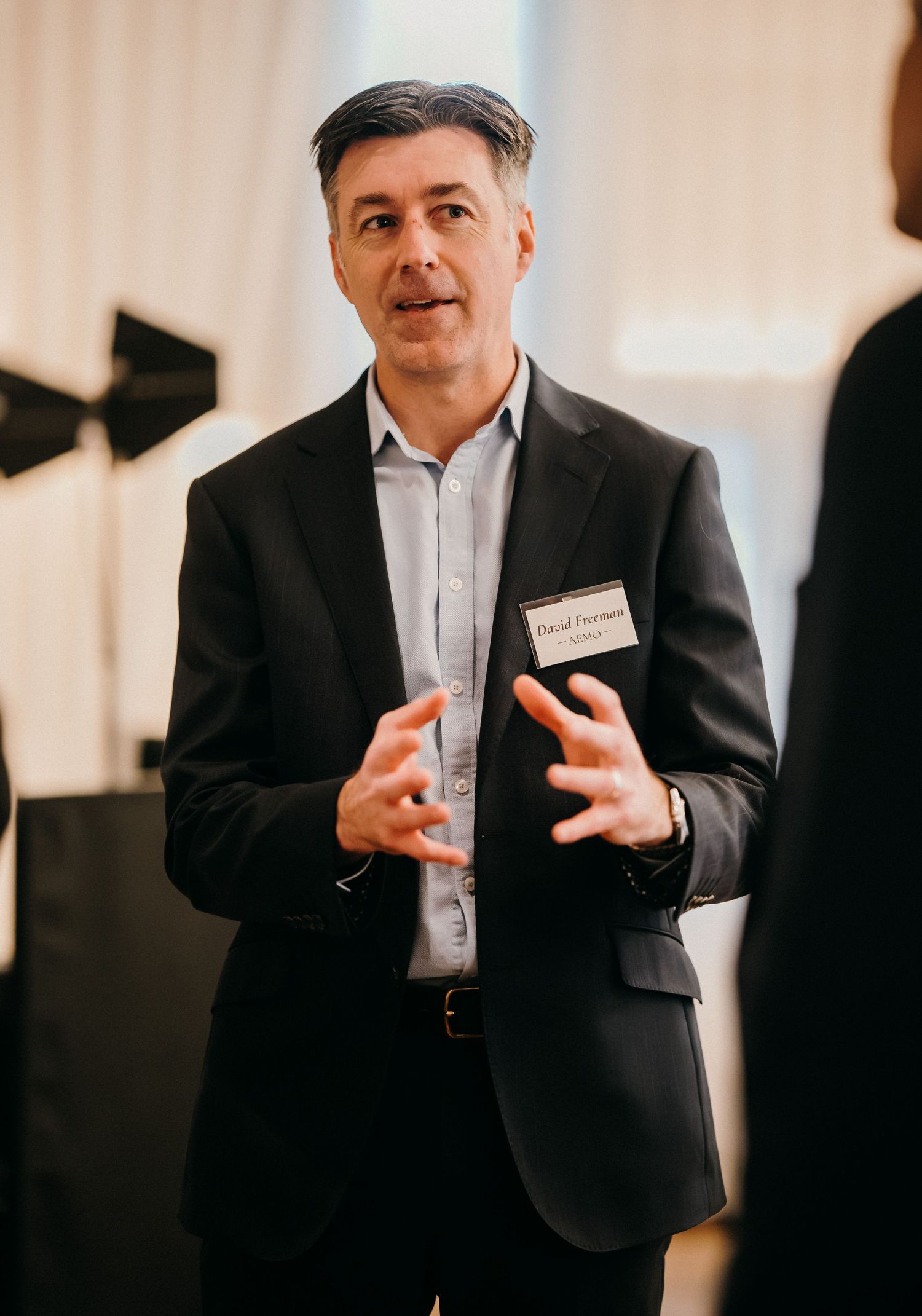 Professional speaker in dark suit gestures while presenting at business conference.