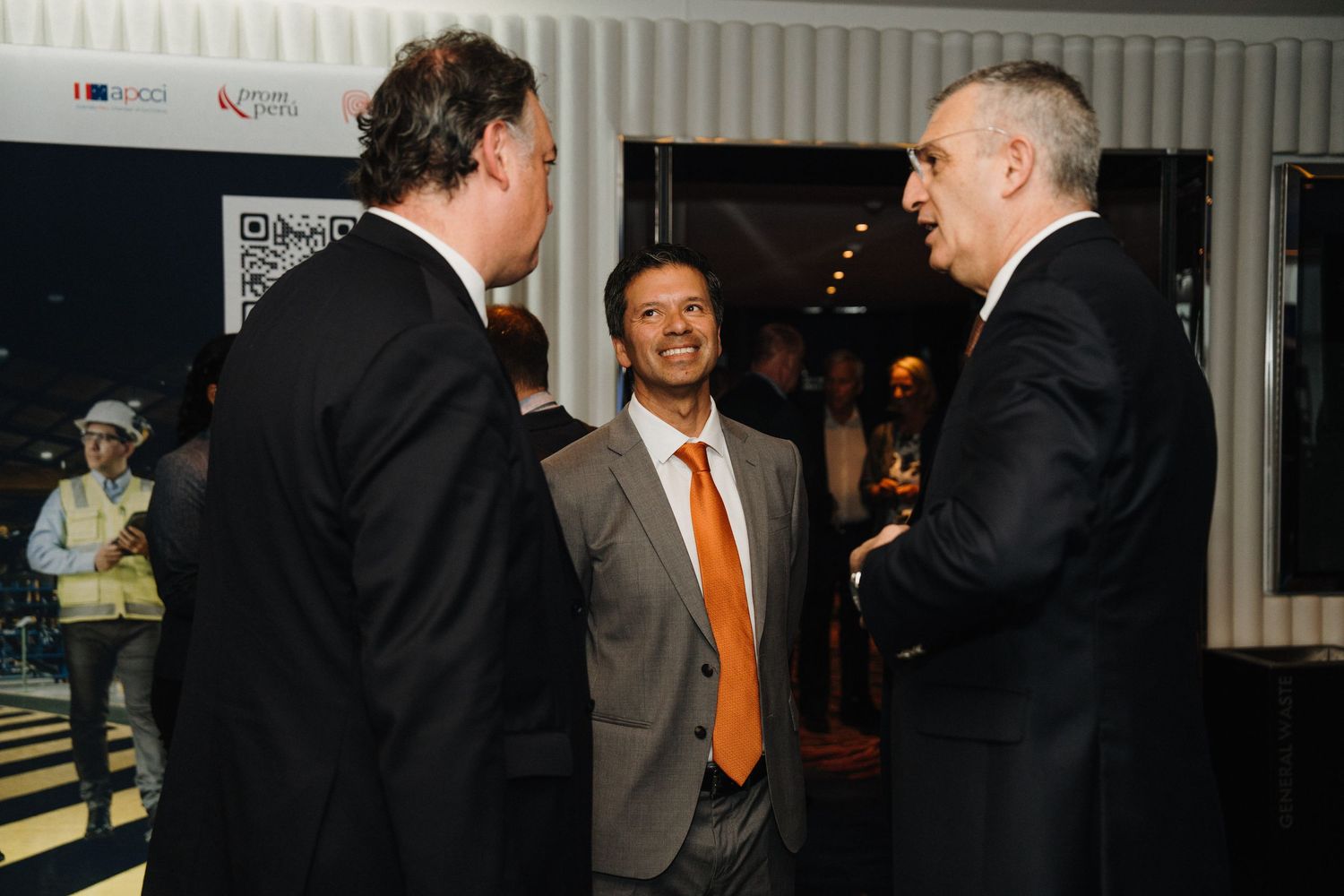 Three people in business attire engaged in animated conversation at what appears to be a professional gathering.