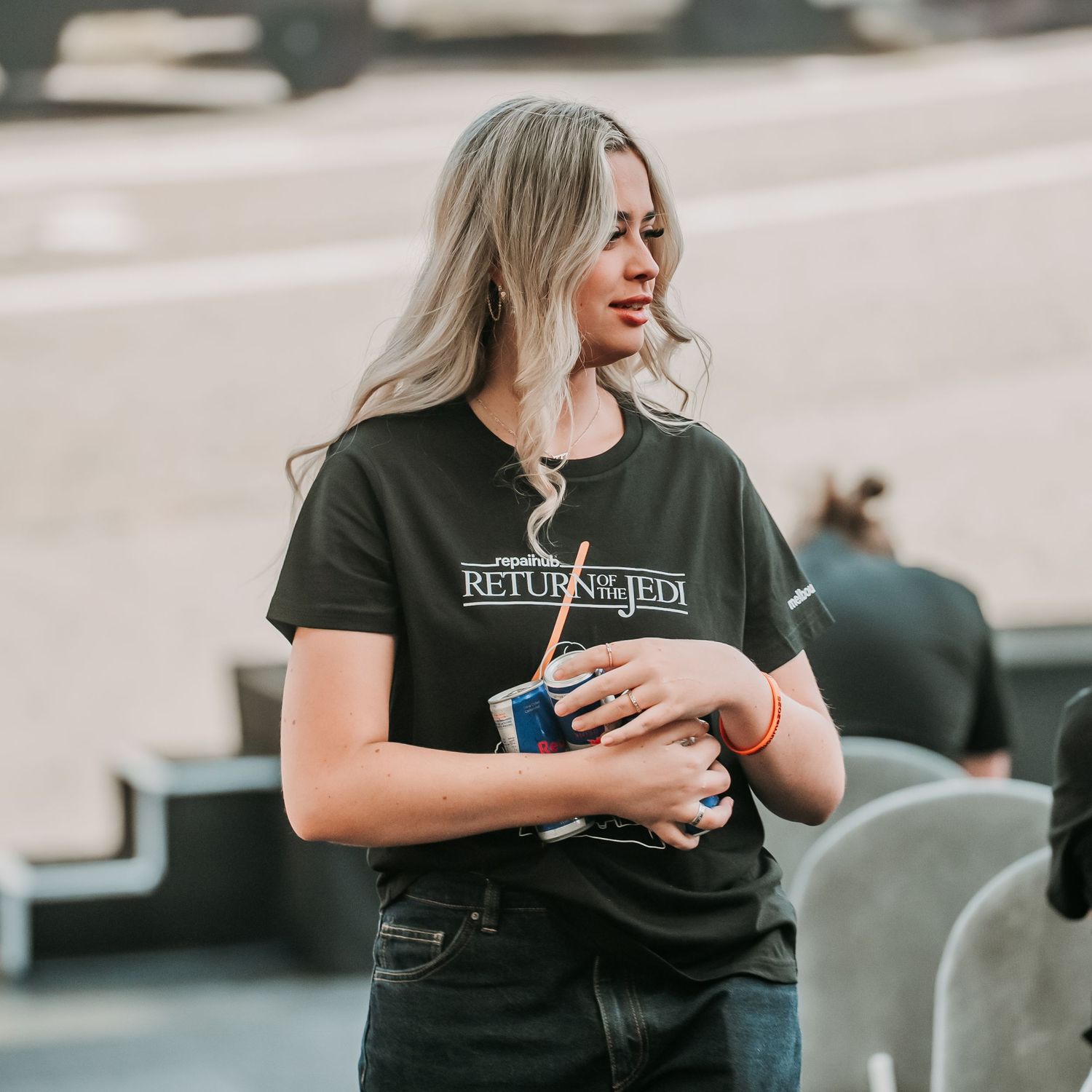 Person in black t-shirt with blonde hair standing in casual pose against light background.