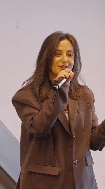 A performer in a brown blazer sings passionately into a microphone while moving energetically on stage.