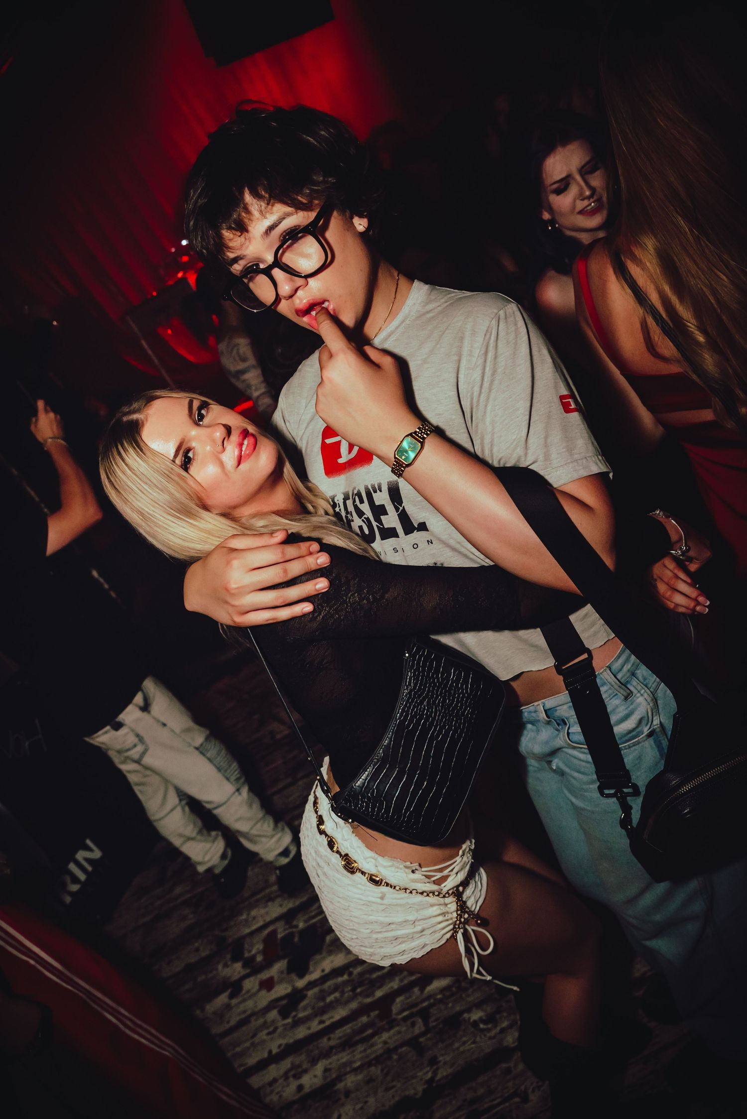 People dancing intimately in a dark nightclub with moody red lighting and atmospheric shadows.