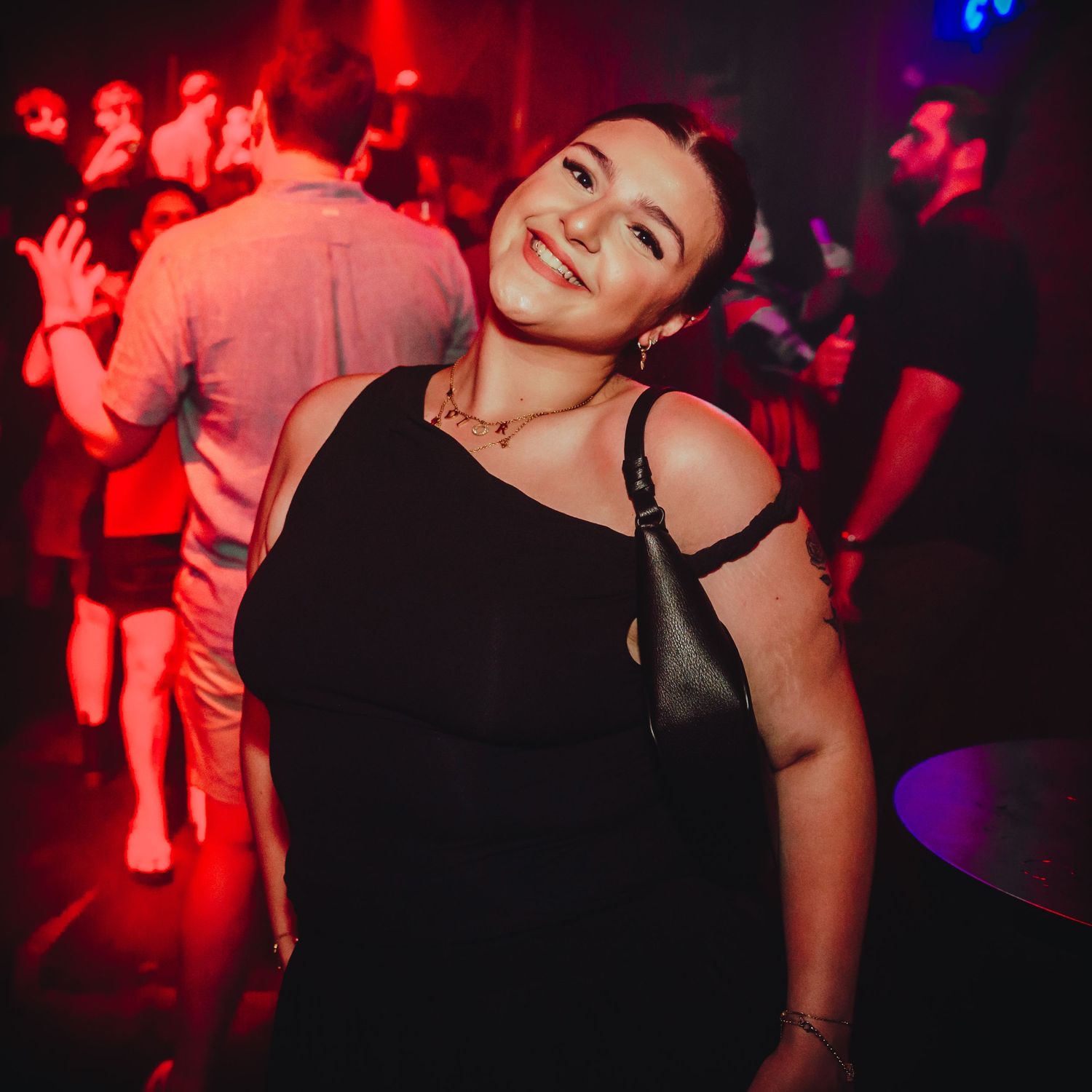 Person in a black sleeveless top dancing and laughing at a nightclub under red and blue lighting.