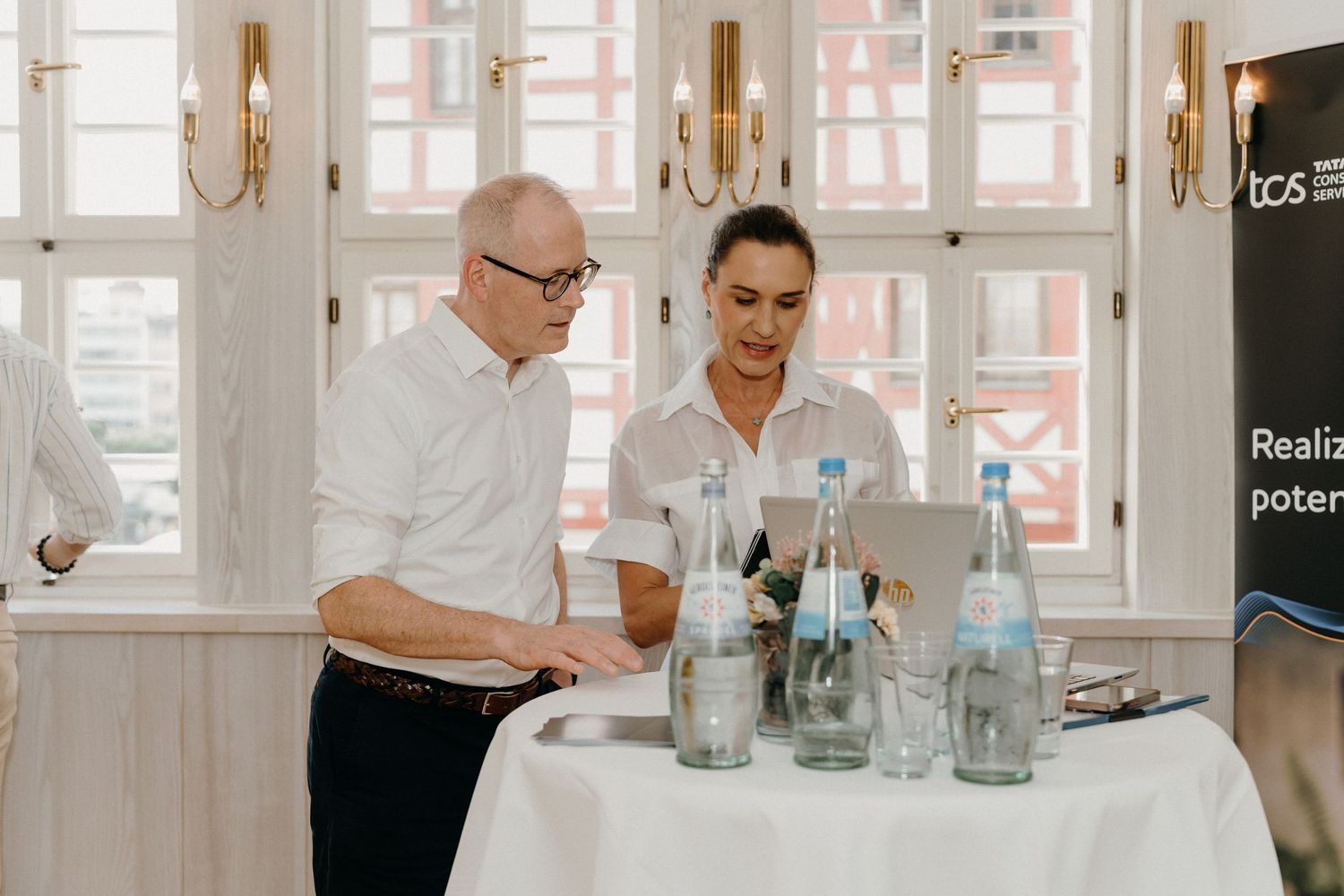 Two professionals reviewing a laptop at a white tablecloth table with water bottles in an elegant conference room.