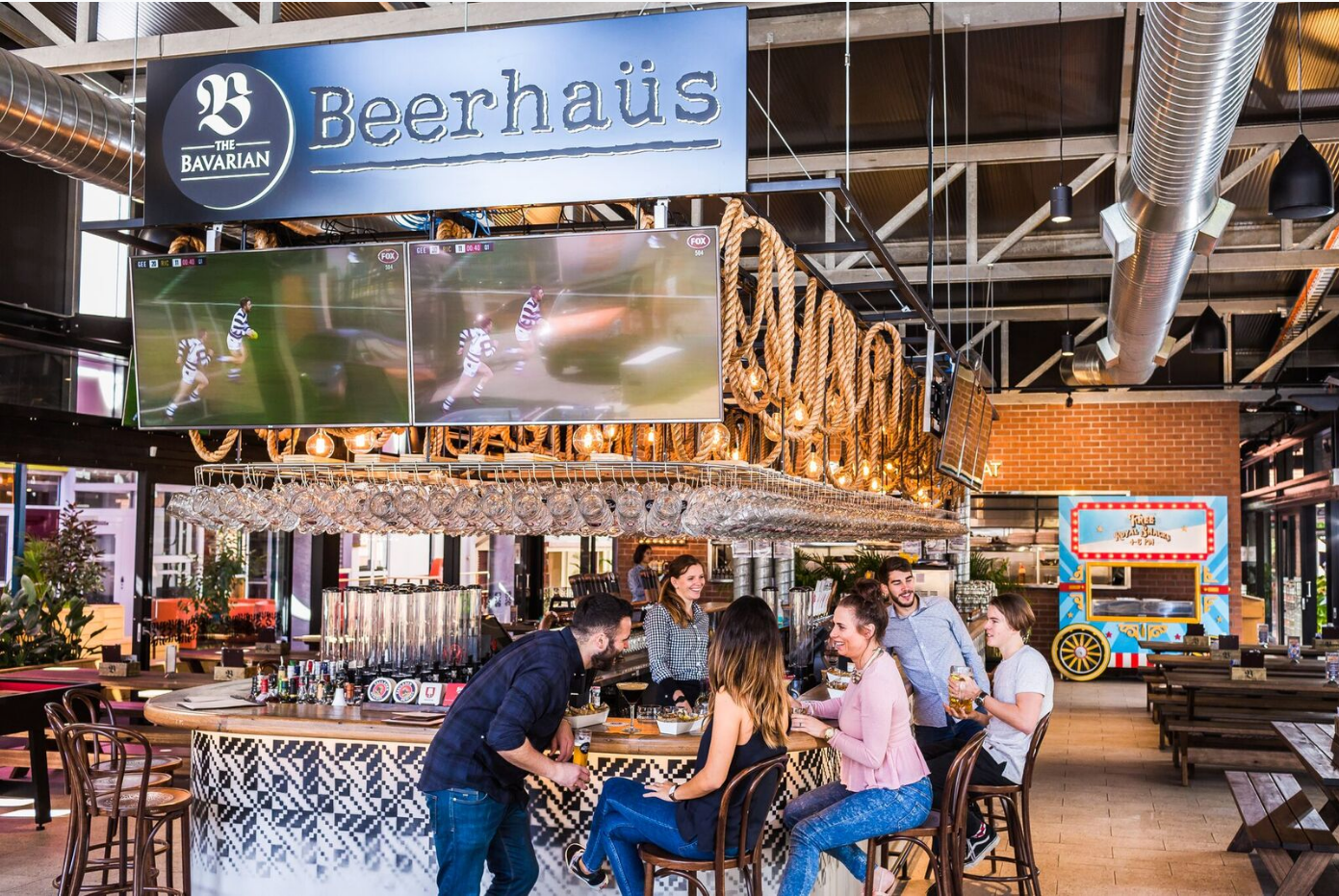 Beer hall interior with long communal tables, rustic wooden decor, and industrial-style lighting in a spacious venue.