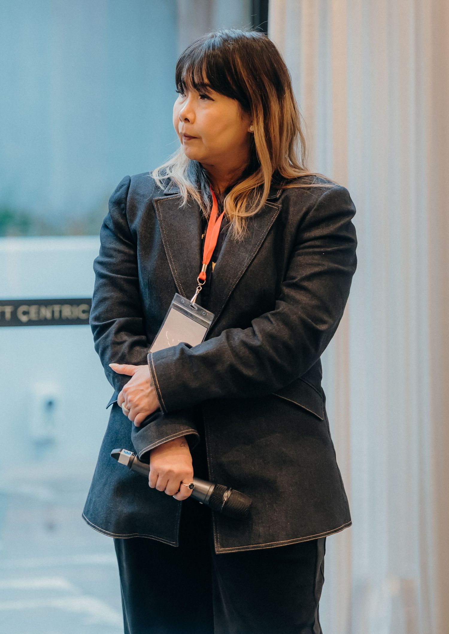 Professional wearing a dark blazer holds a folder while walking in a business setting.