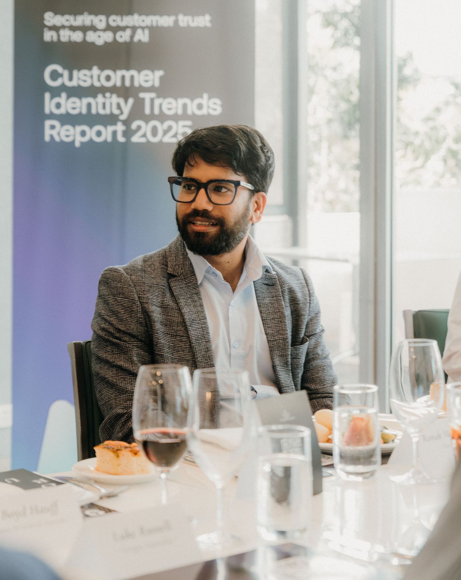 Business professionals seated at a conference table with wine glasses during a customer identity trends presentation.