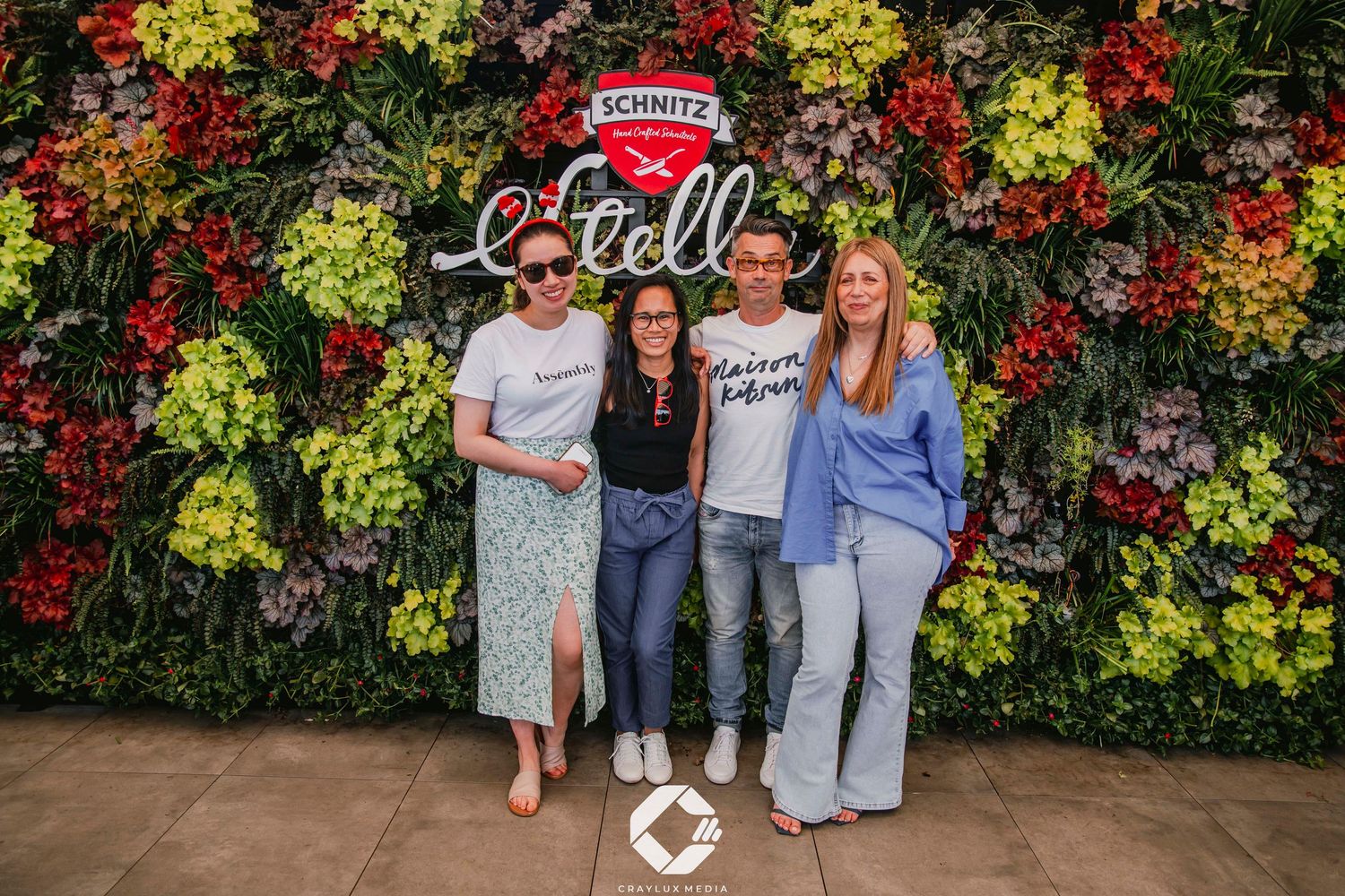 A group poses together in front of a vibrant wall covered with colorful autumn flowers and greenery.
