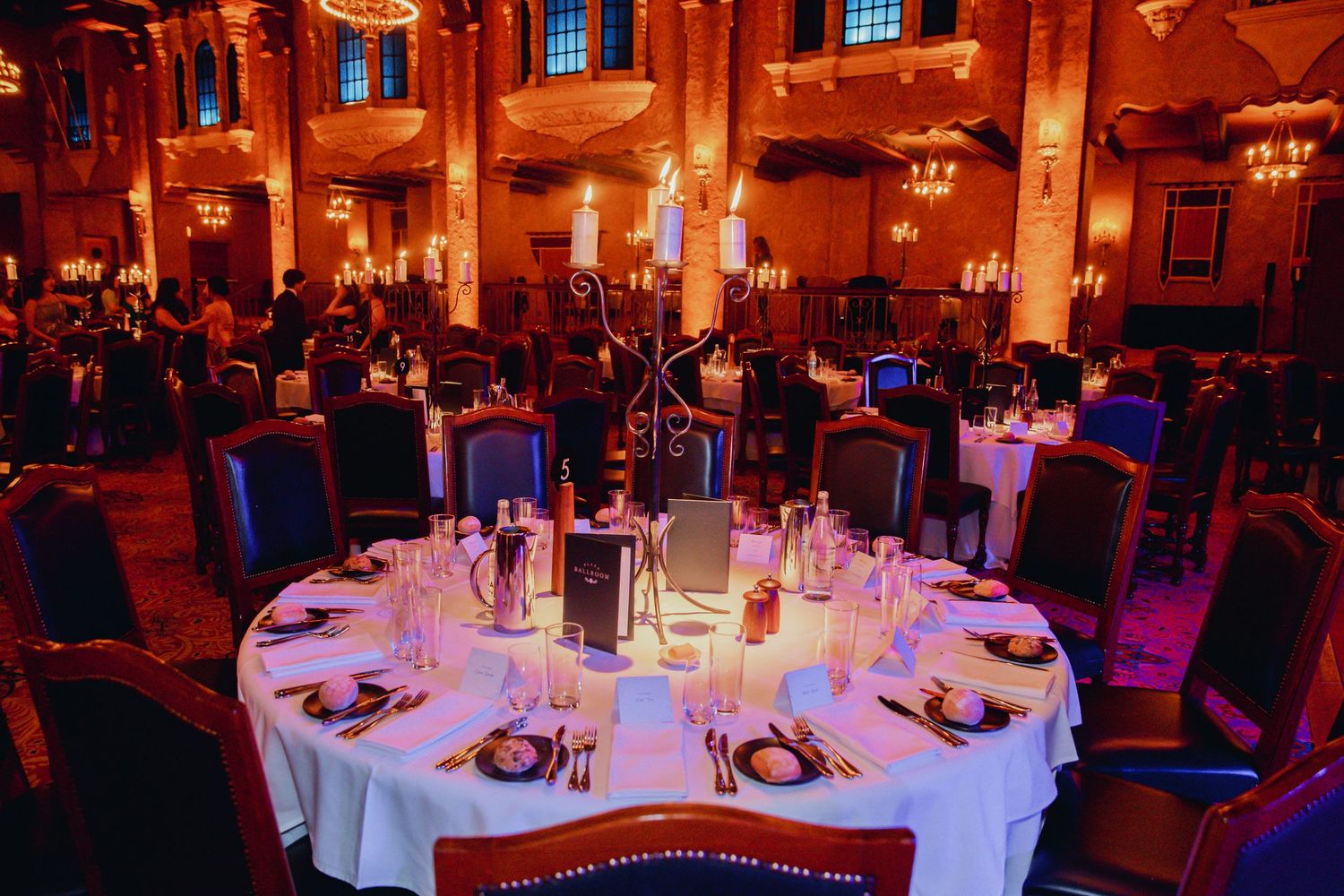 Elegant wedding venue setup with circular tables, centerpieces and dramatic red-orange ambient lighting in historic setting.