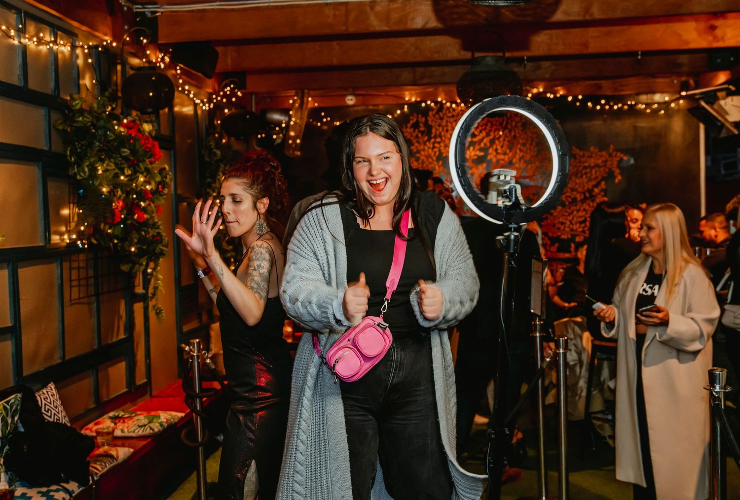 Wedding guests dancing and celebrating at a dimly lit reception venue decorated with string lights and holiday greenery.
