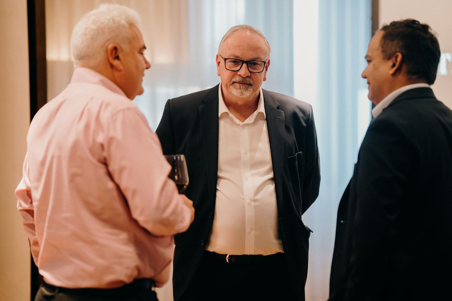 Three business professionals engaged in conversation during a networking event in a bright indoor setting.