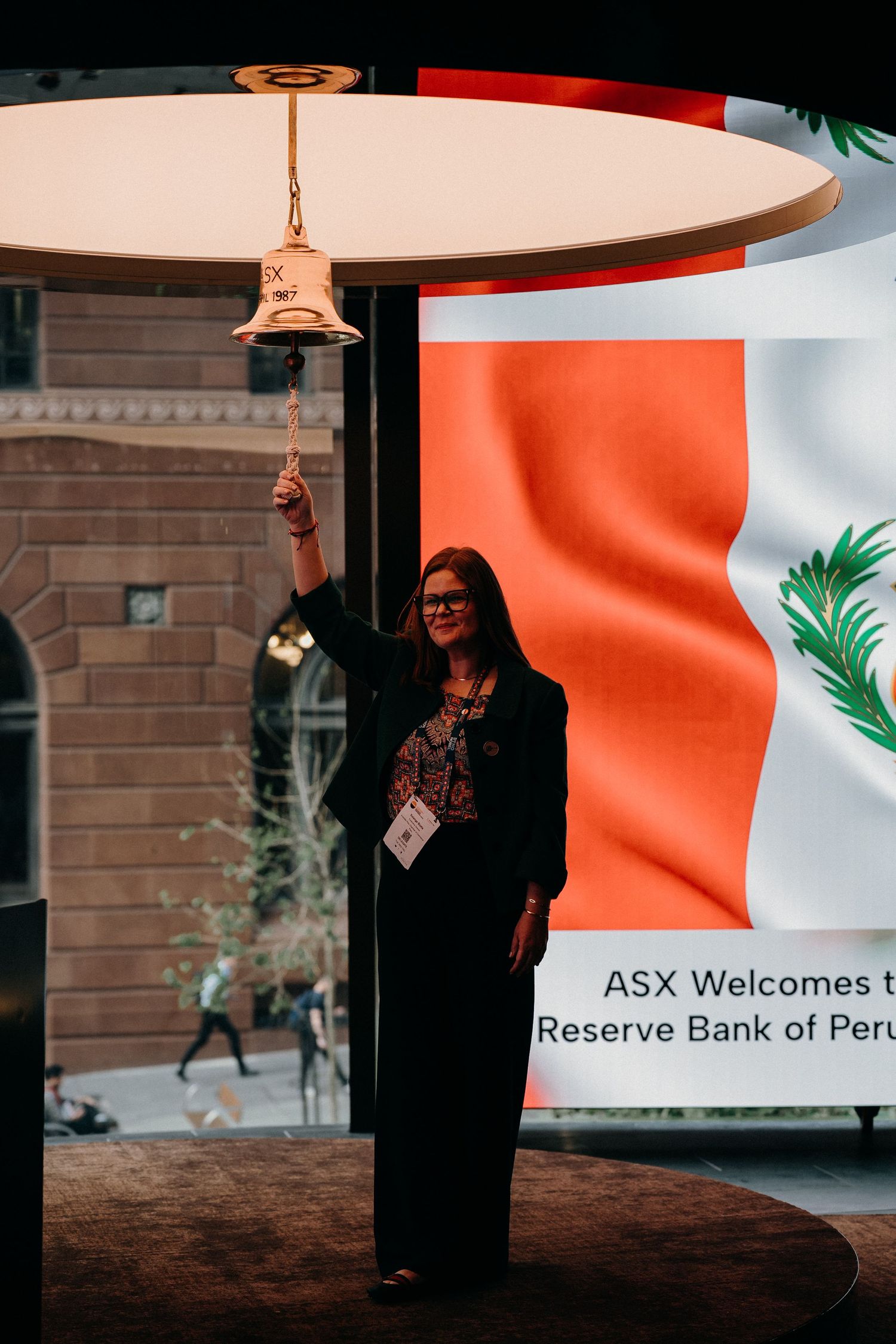 Professional figure stands against backdrop of Peruvian flag at Reserve Bank event with ASX welcome signage visible.
