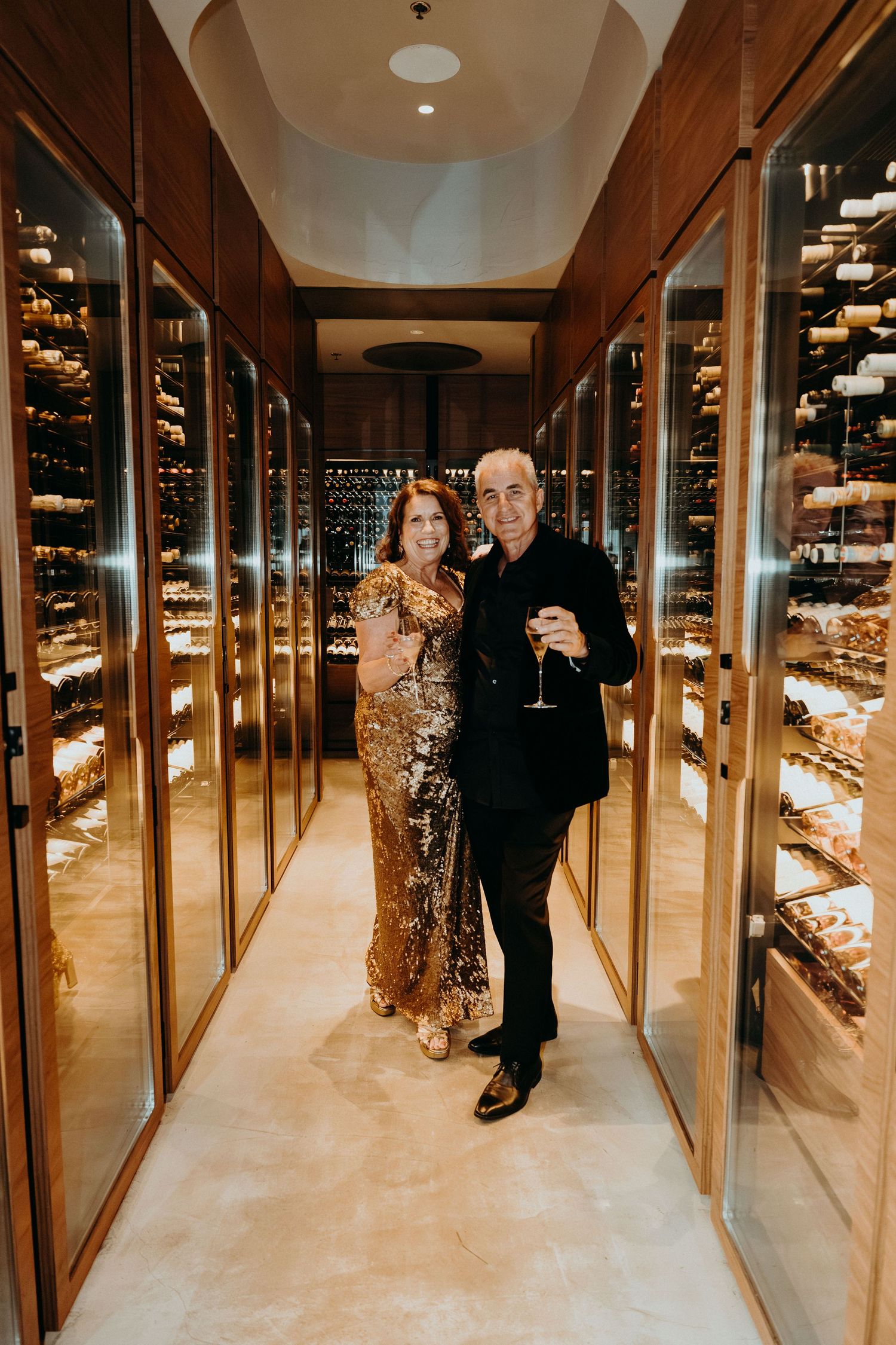 Elegant couple reflected in mirrored hallway with wine display cases creating an infinite reflection effect.