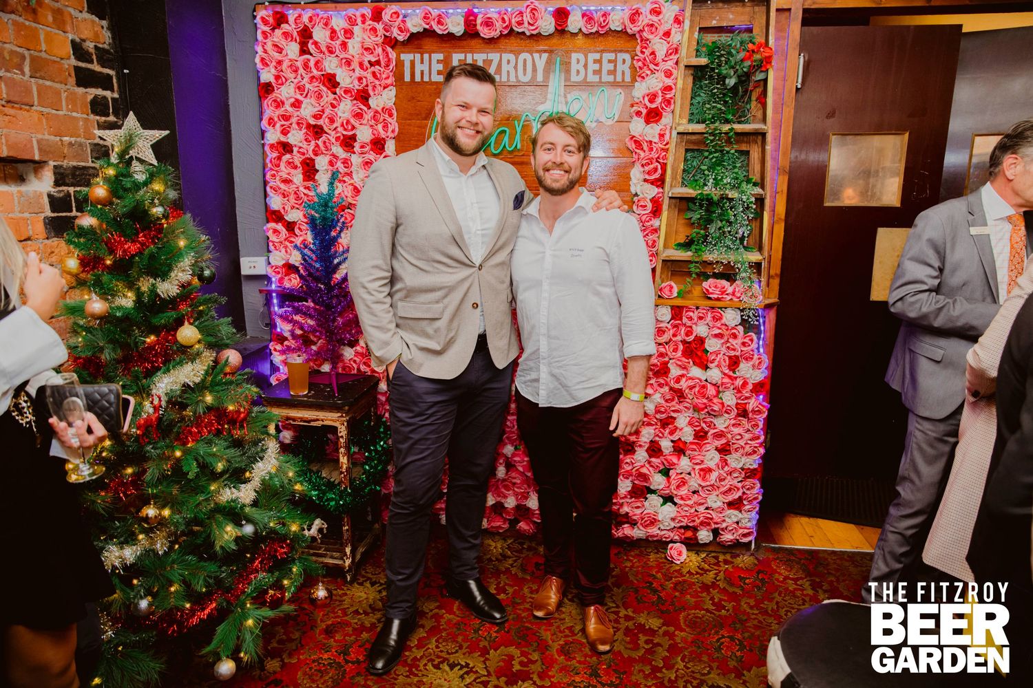 A festive holiday party scene with a decorated Christmas tree and red floral backdrop for photos.