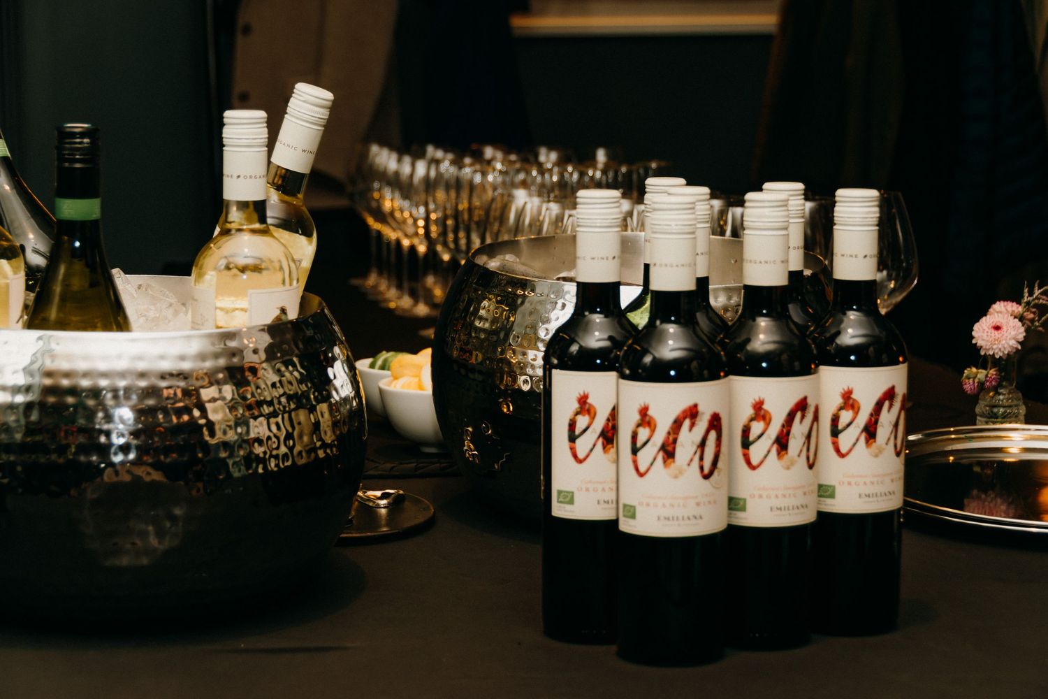 Assorted wine bottles and glassware displayed on wooden shelves in a dimly lit bar or restaurant setting.