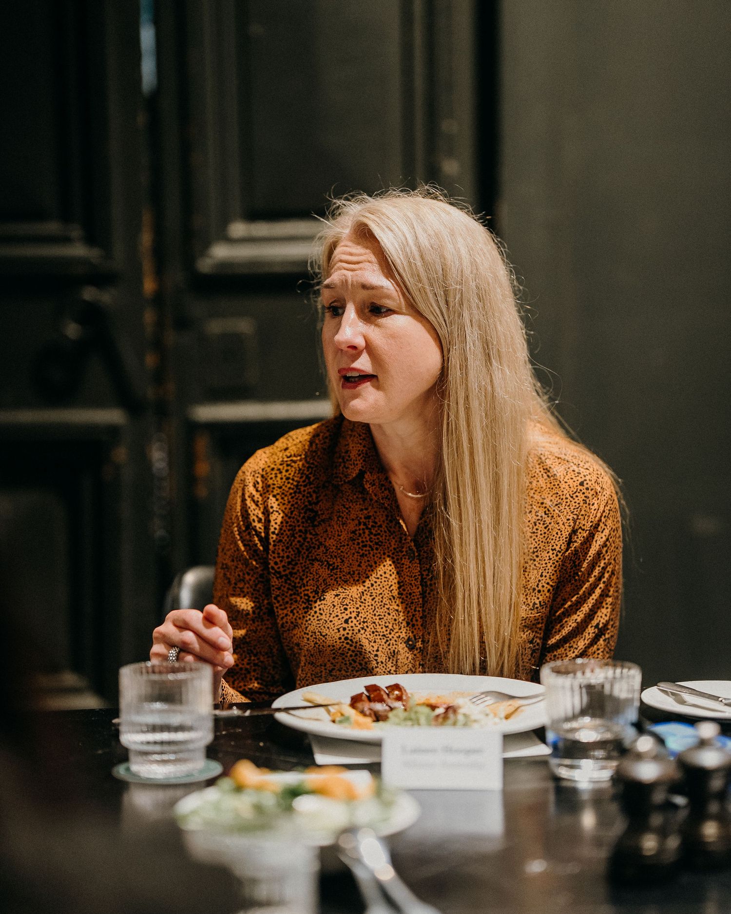 A person in a mustard-colored top dines at a restaurant table with water glasses and plates of food.