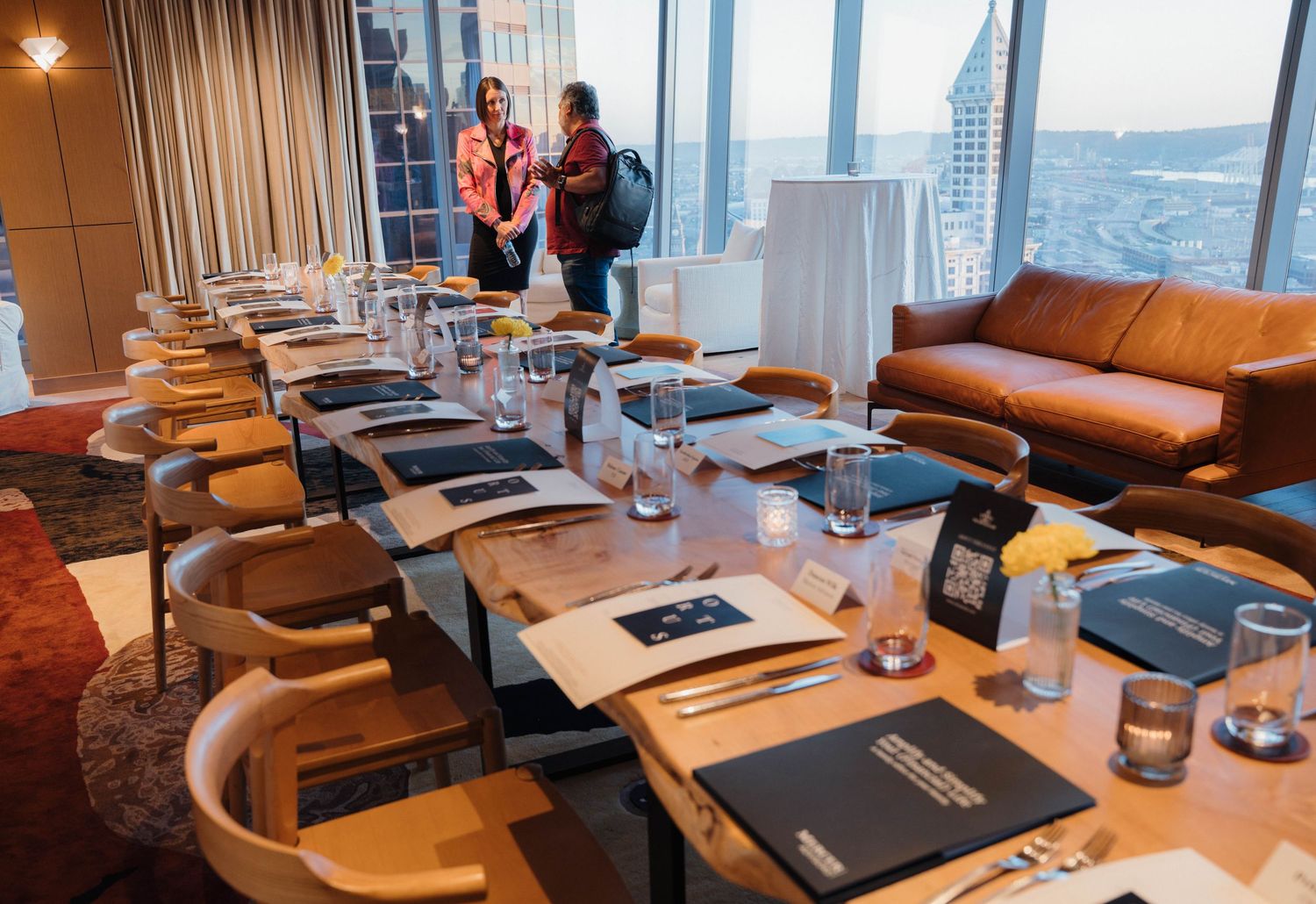 Modern restaurant interior with curved leather booths and wooden tables arranged along windows with city views.