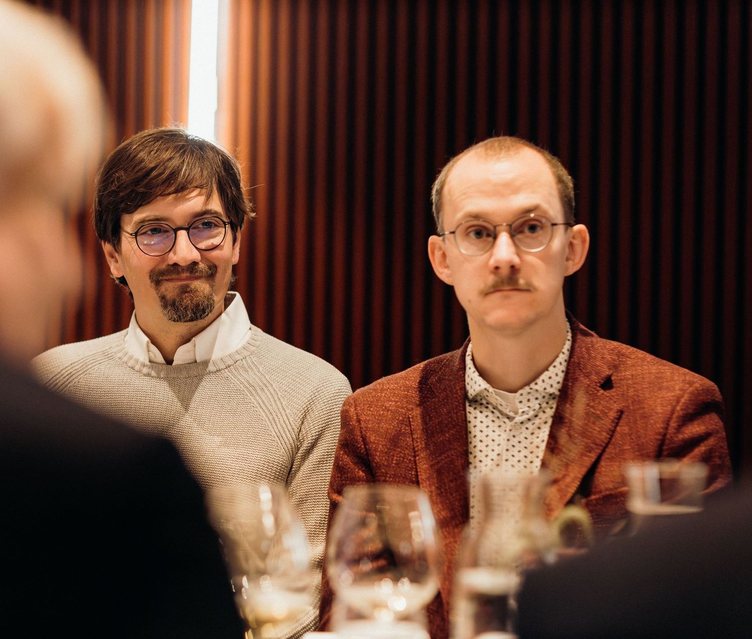 A group of people sitting at a dining table in formal attire during an indoor gathering.