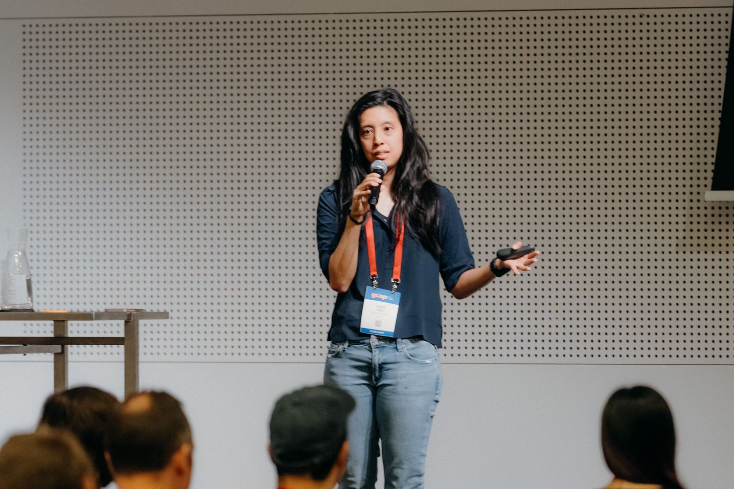 A presenter gestures while speaking to an audience during a professional conference presentation.