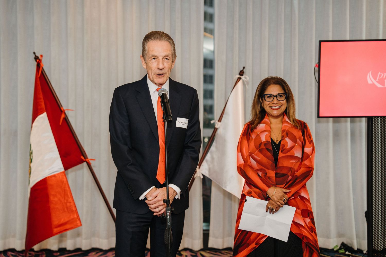 Business professionals in formal attire gather for a meeting in a modern conference room with Canadian flags visible.