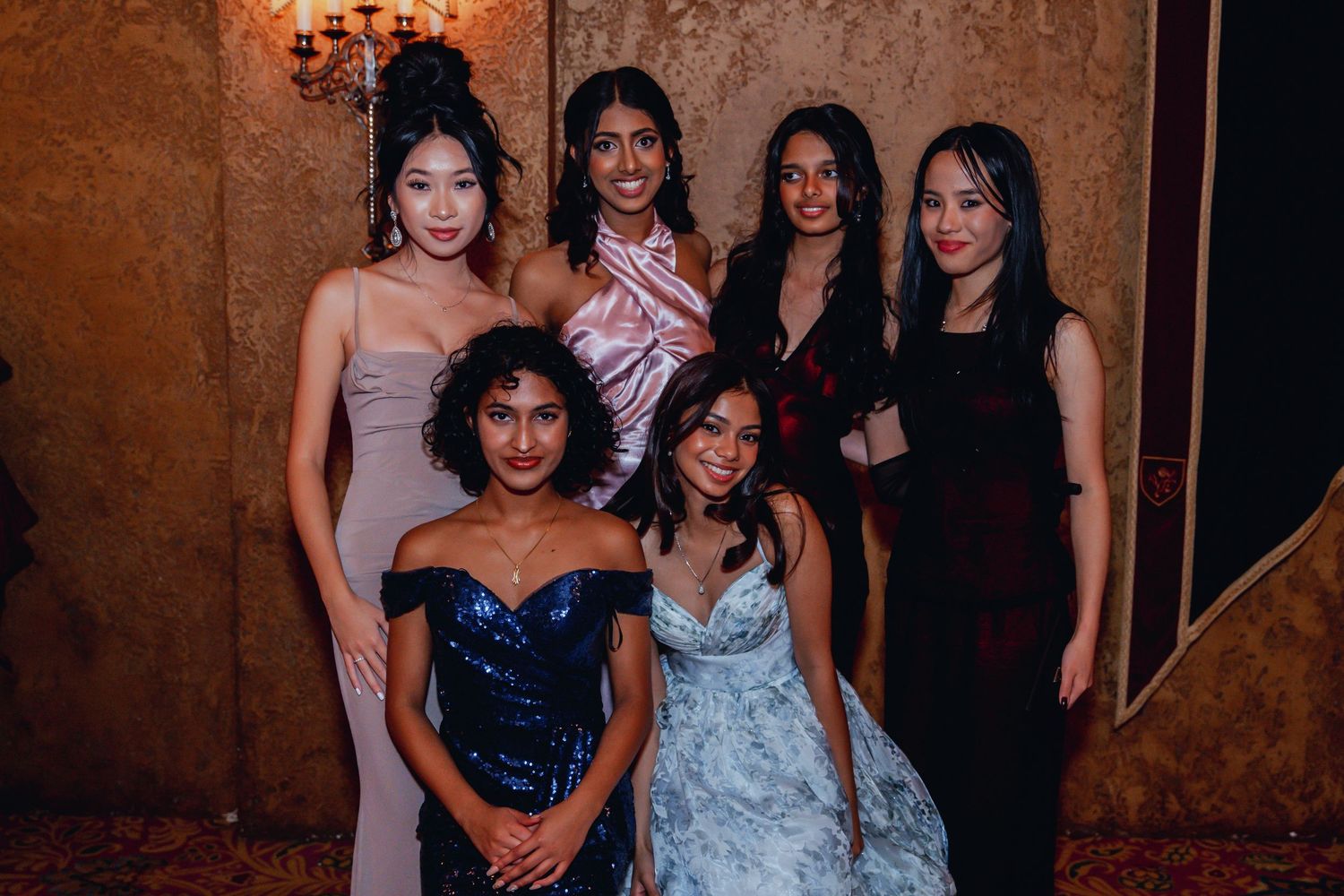 A group of elegantly dressed women posing together at a formal event in evening gowns and cocktail dresses.