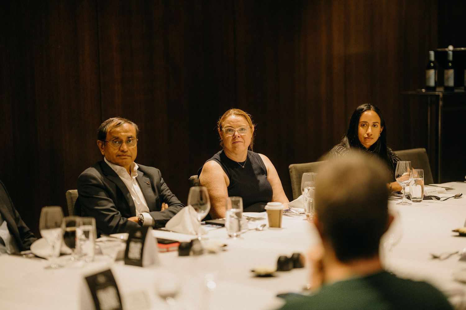 Three professionals seated at a formal dining table during a business dinner event in an elegant venue.
