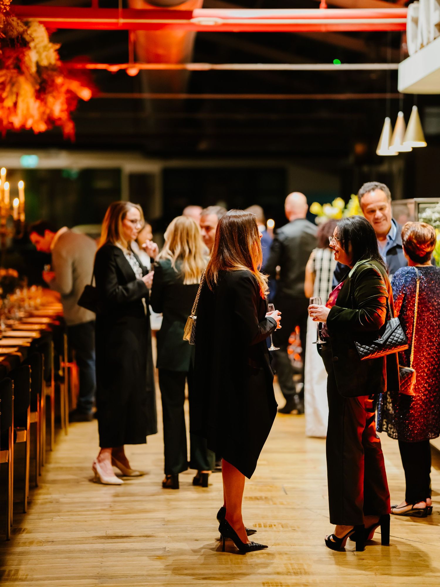 People in formal attire gather in church pews during a wedding ceremony with warm autumn lighting.