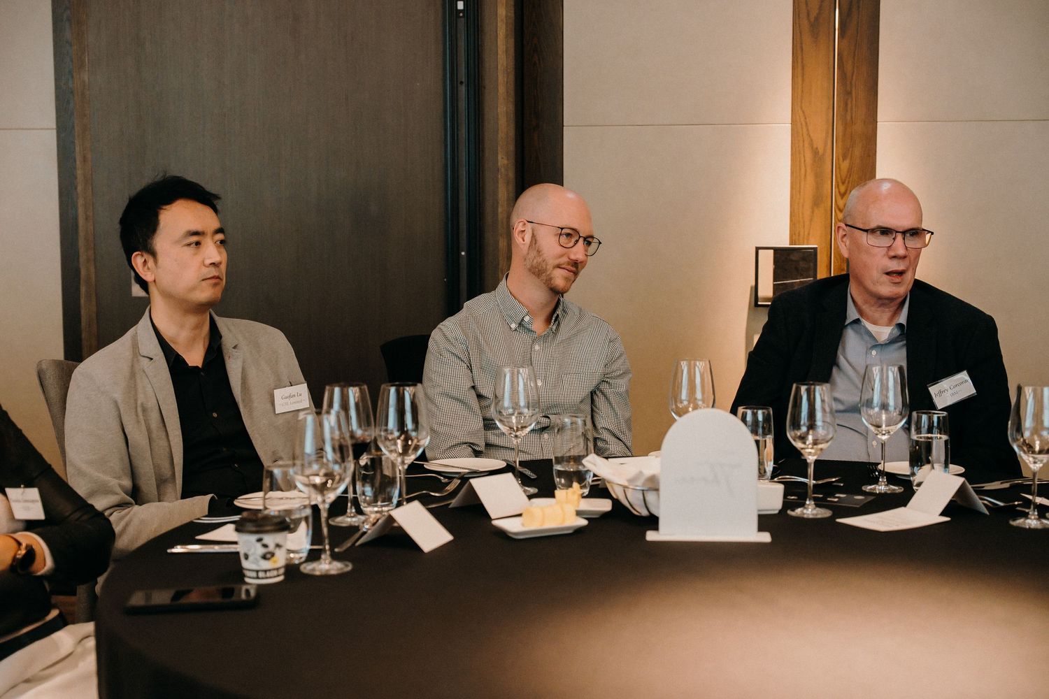 Business professionals hold a dinner meeting at a long table in a conference room setting.