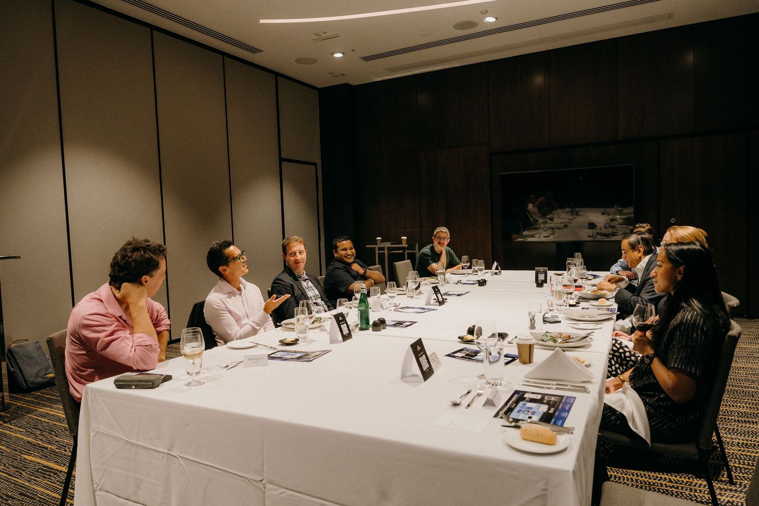 Business professionals gathered around a white conference table for a formal dinner meeting in a modern hotel boardroom.