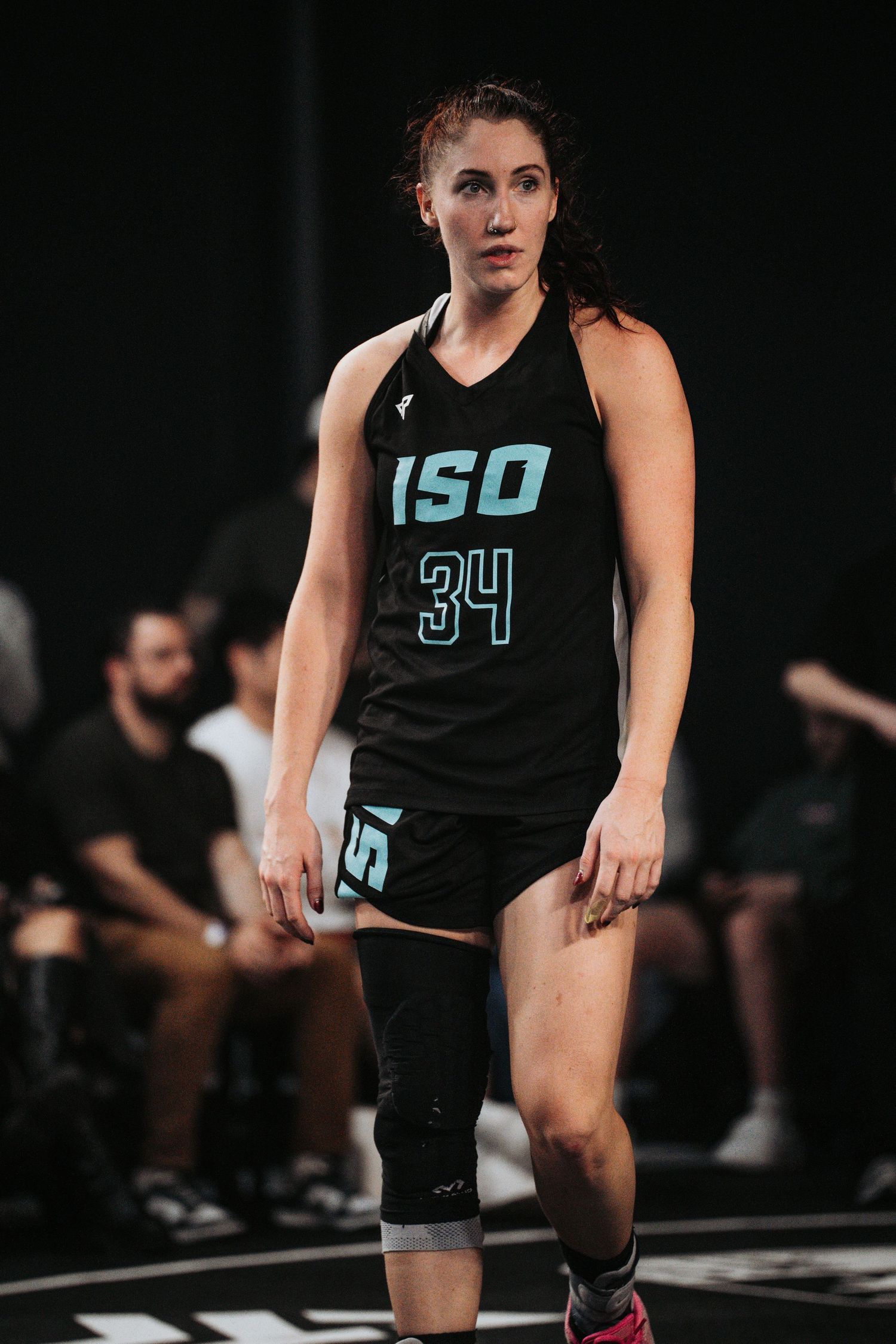Basketball player in black ISO jersey number 34 stands on court with knee brace during game.